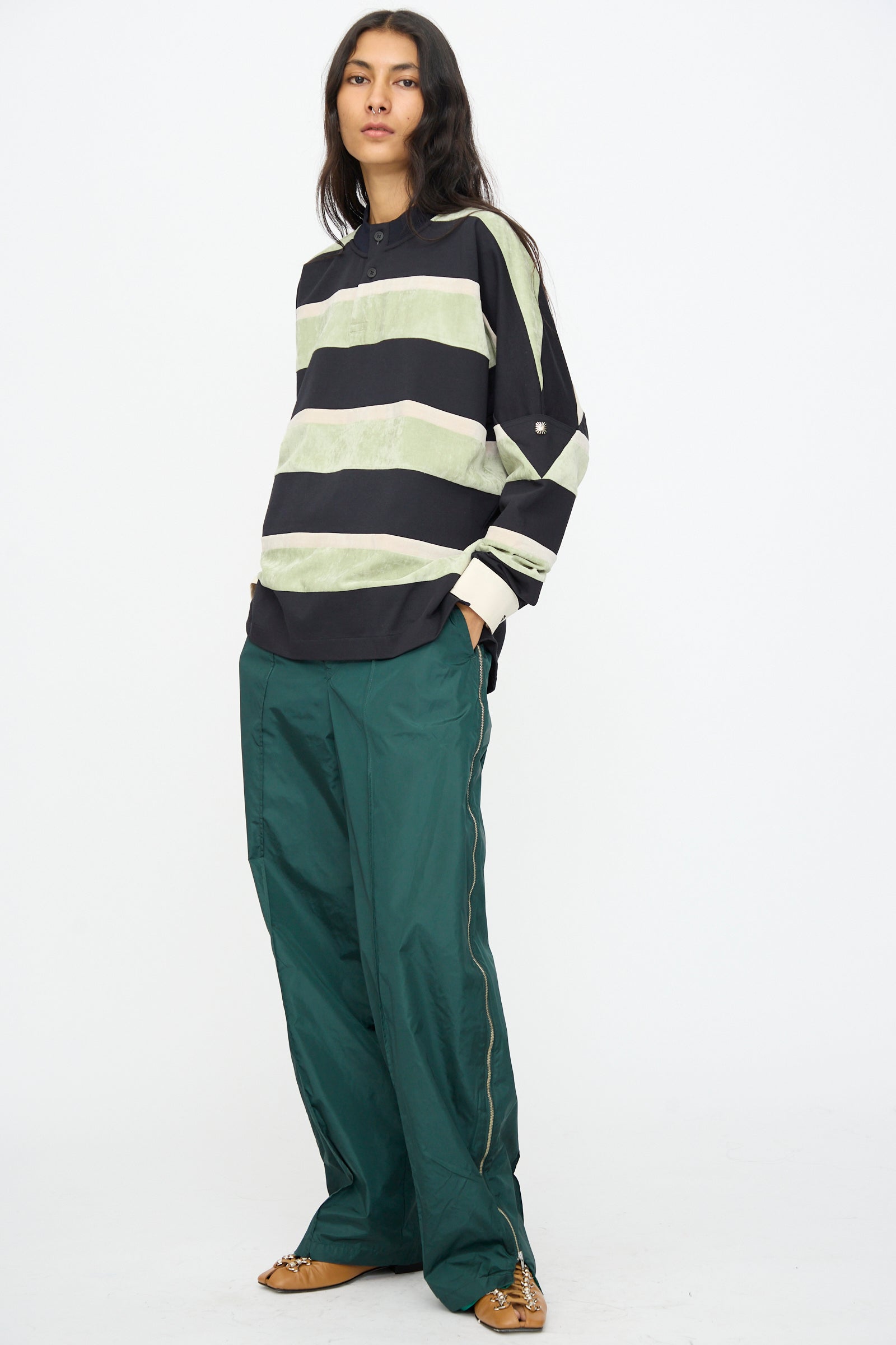 A person stands against a plain background wearing the TOGA ARCHIVES Velvet Border Jersey Long Sleeve in Light Green, paired with green wide-leg pants and brown shoes.