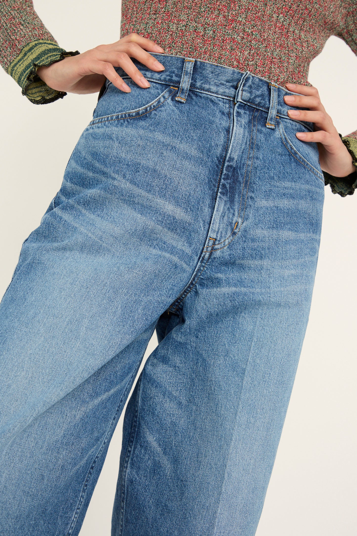 A person is wearing TOGA ARCHIVES' Wide Denim Pant in Blue and a knitted top, with hands on hips, seen from from the waist down.