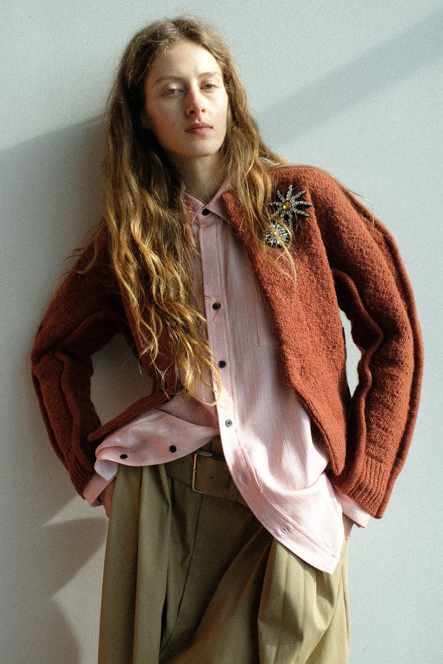 A woman leaning against a wall wearing pieces from Toga Archives FW25 collection with her hands in her pocket.