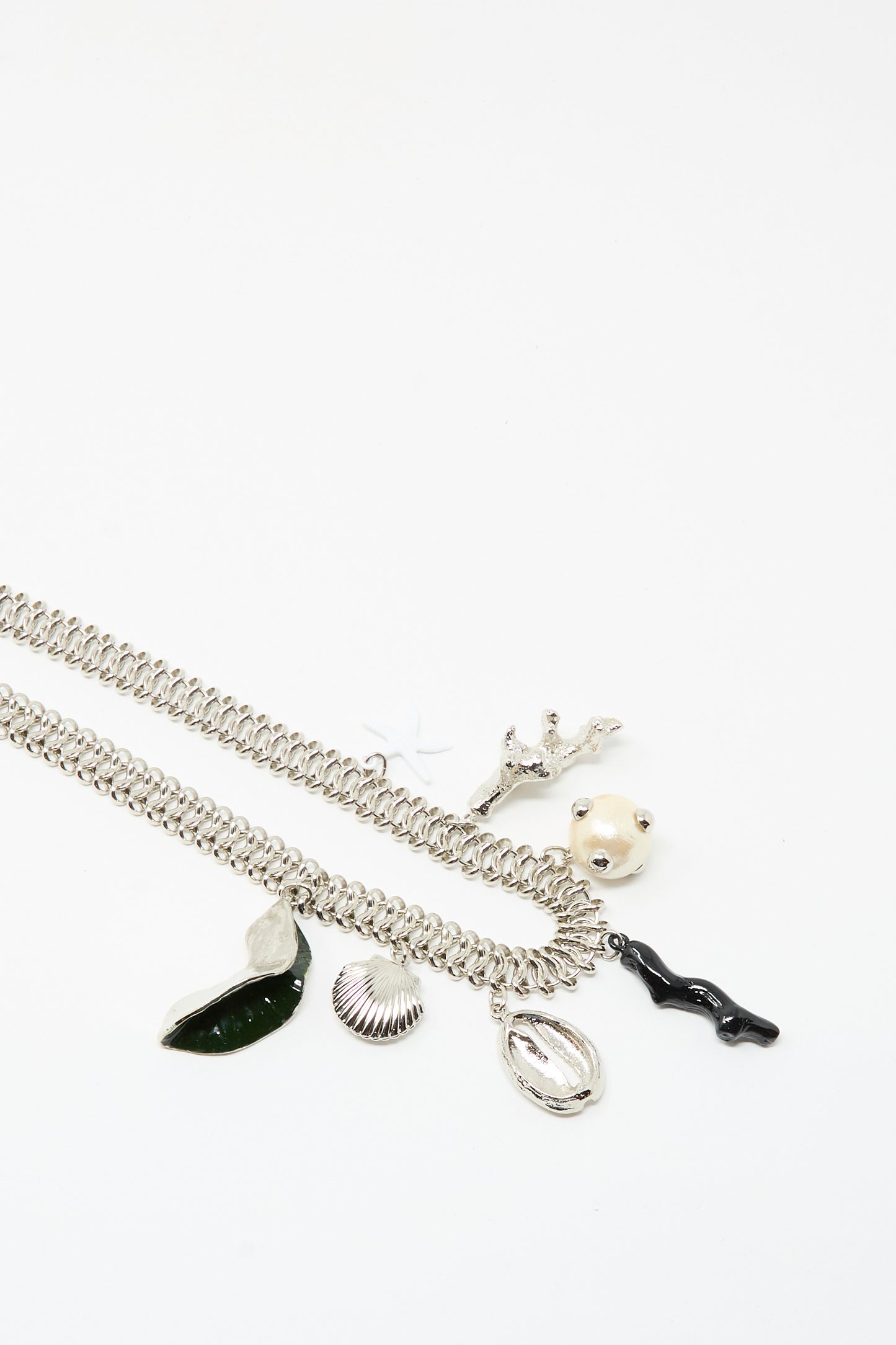 The Motif Necklace in Silver by TOGA ARCHIVES features a silver chain with a toggle clasp and five unique charms—a leaf, shell, branch, round face, and wavy black form—shown against a white background.