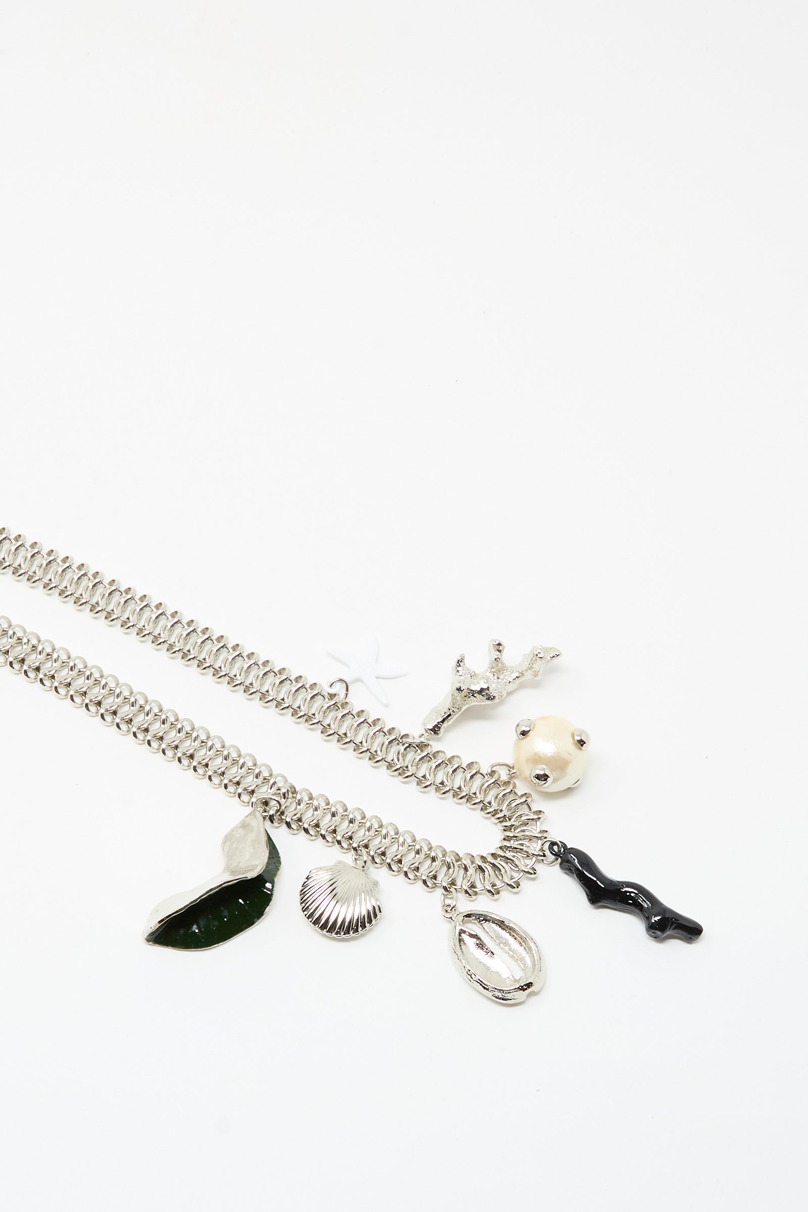 The Motif Necklace in Silver by TOGA ARCHIVES features a silver chain with a toggle clasp and five unique charms—a leaf, shell, branch, round face, and wavy black form—shown against a white background.