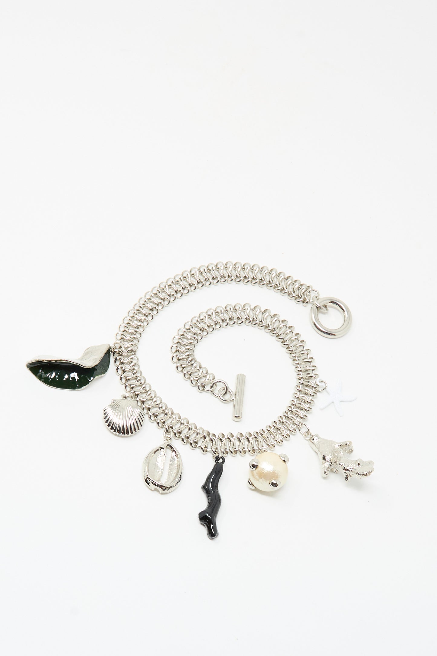 The Motif Necklace in Silver by TOGA ARCHIVES features six unique charms—green whale tail, shell, cowrie shell, black figure, pufferfish, and white coral—on a silver chain with a secure toggle clasp for easy wear.