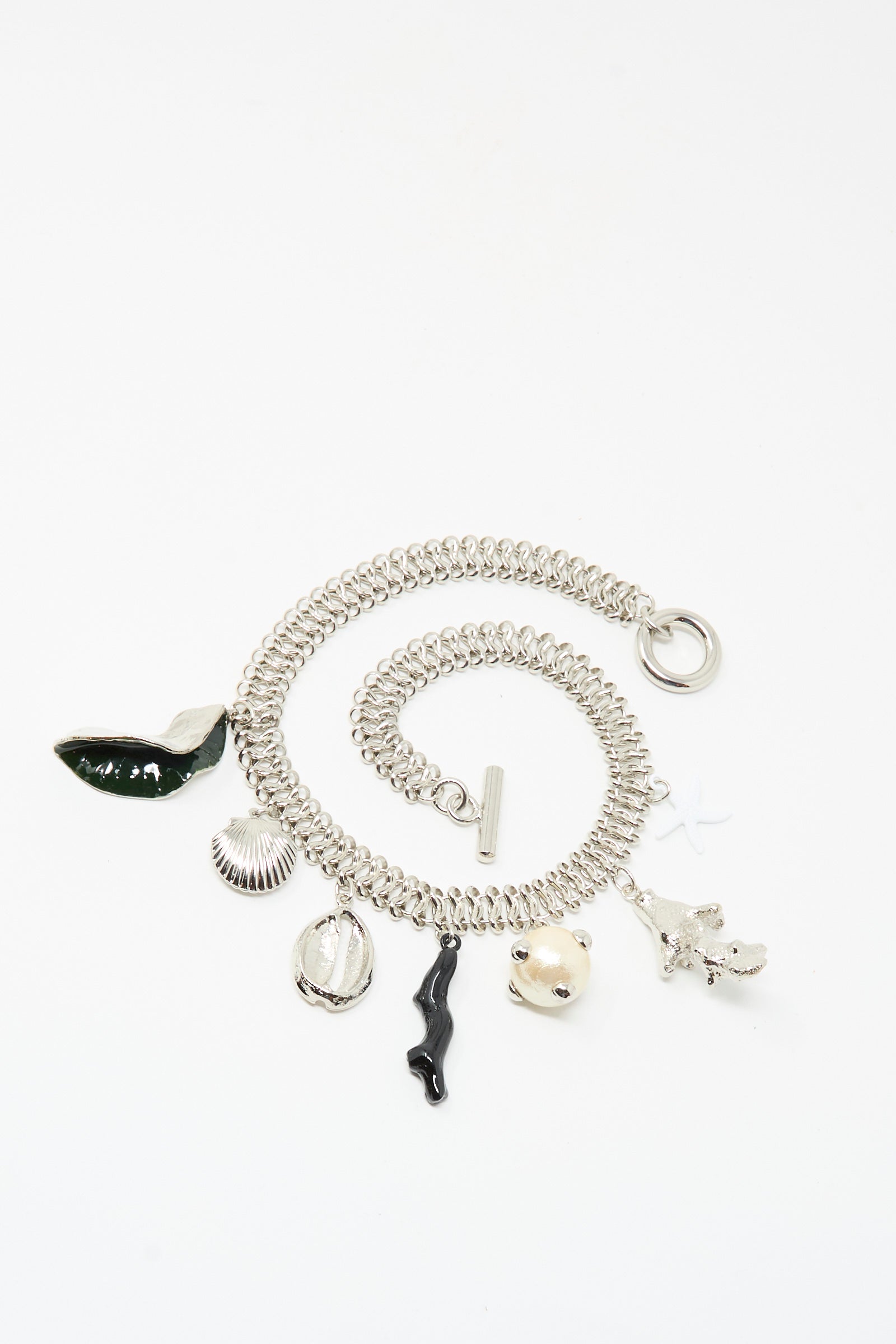 The Motif Necklace in Silver by TOGA ARCHIVES features six unique charms—green whale tail, shell, cowrie shell, black figure, pufferfish, and white coral—on a silver chain with a secure toggle clasp for easy wear.