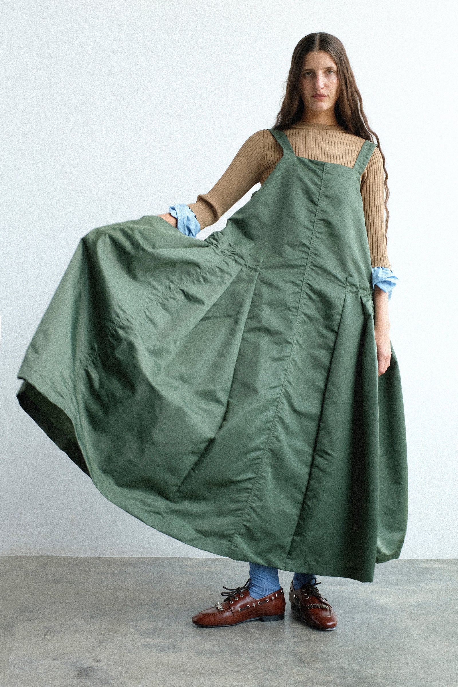 A woman wearing Toga Archives Nylon Twill Dress in Khaki standing against a plain light gray wall.