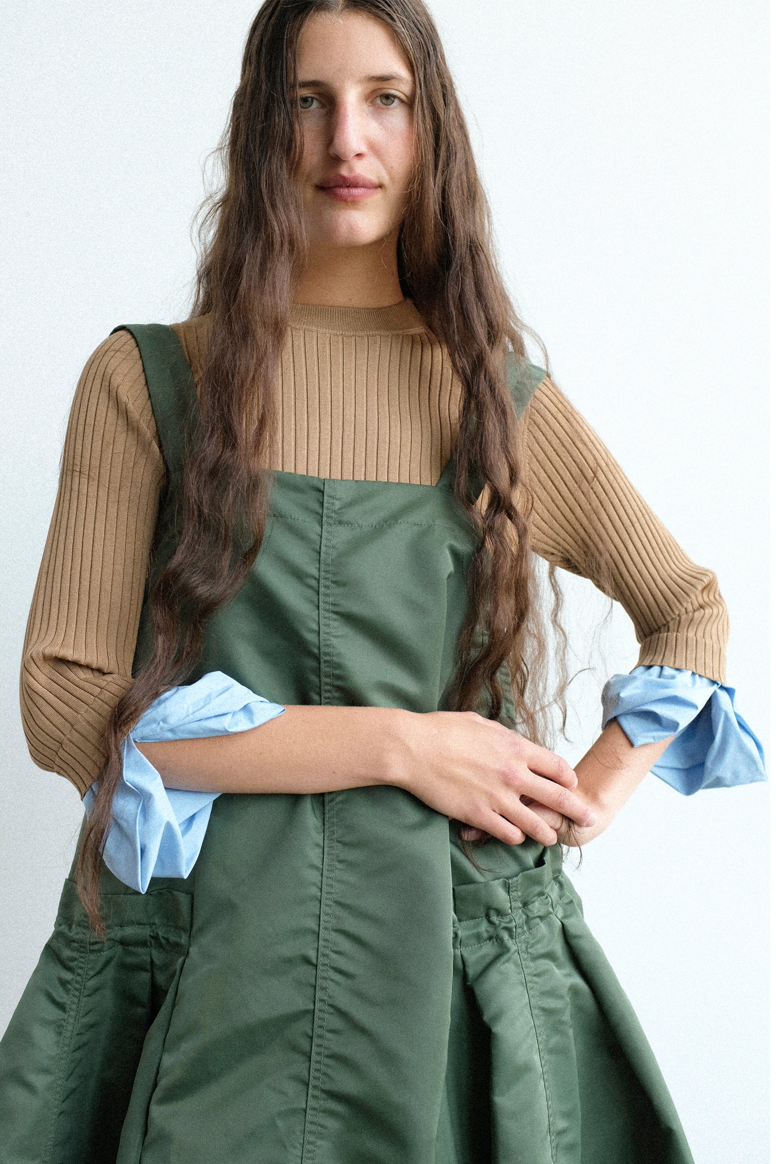 A woman wearing  the Toga Archives Rib Knit Top in Camel, with the Nylon Twill Dress in Khaki over photographed against a plain light background.
