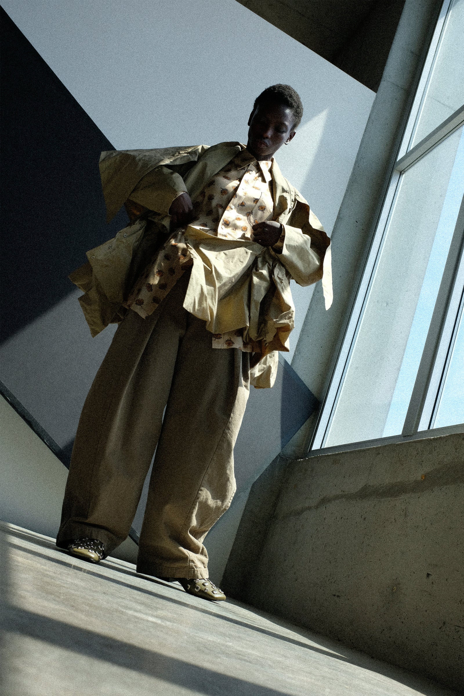 Person wearing Toga Archives Memory Taffeta Jacket in Beige, Flower Print Shirt in Beige, and the Oxford Wide Pants in Beige in an indoor setting.
