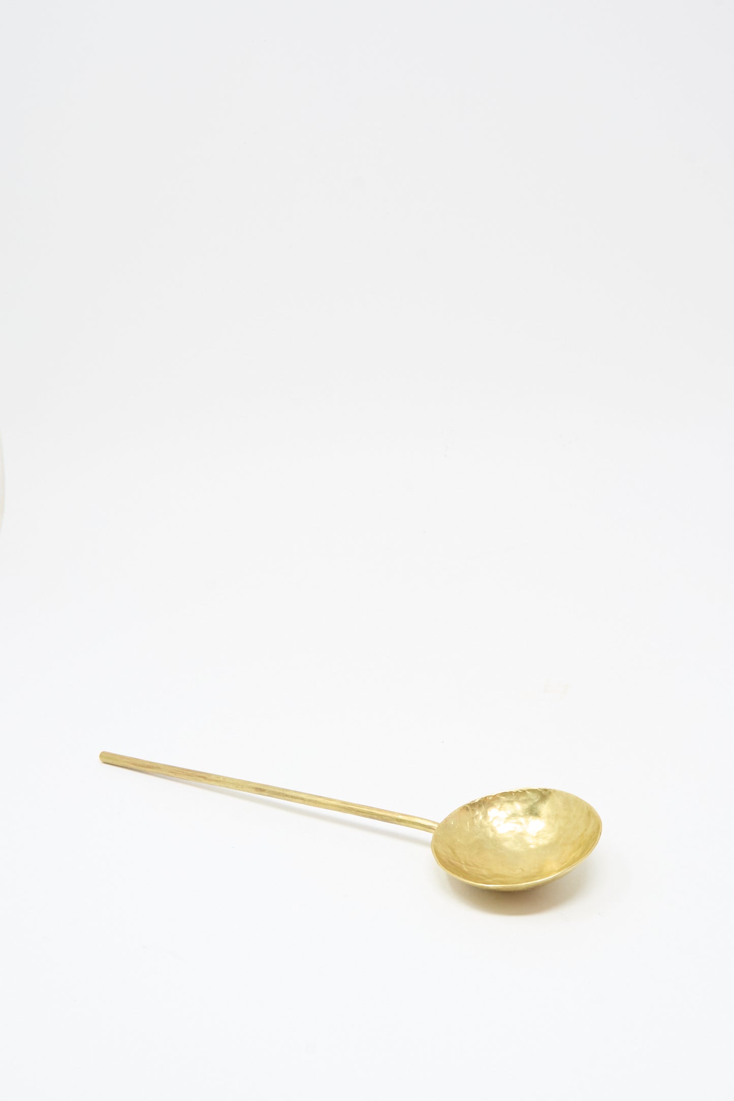 The Totem Home Brass Serving Spoon, handcrafted in Portugal with a long handle, is displayed on a plain white background.