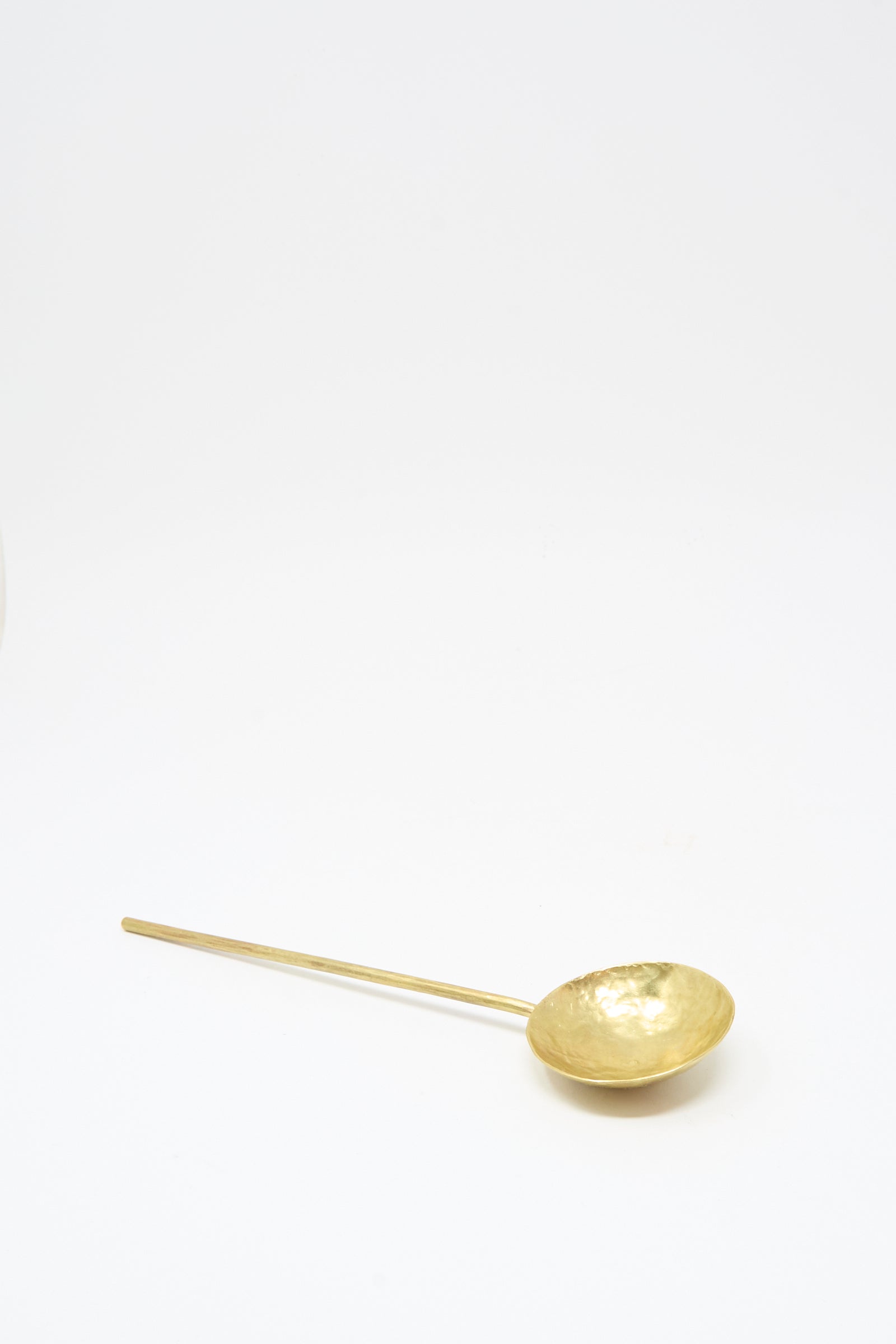 The Totem Home Brass Serving Spoon, handcrafted in Portugal with a long handle, is displayed on a plain white background.