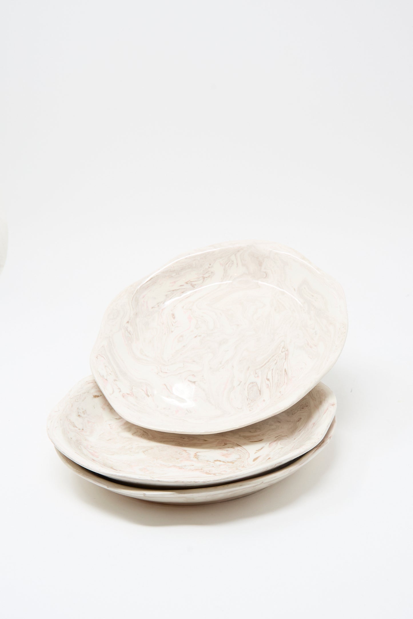 Three Totem Home Wild Rose Shallow Bowls, featuring an off-white ceramic base with a marbleized pink glaze, are stacked on a plain white background.