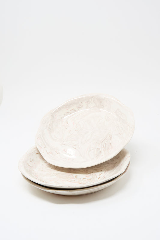 Three Totem Home Wild Rose Shallow Bowls, featuring an off-white ceramic base with a marbleized pink glaze, are stacked on a plain white background.