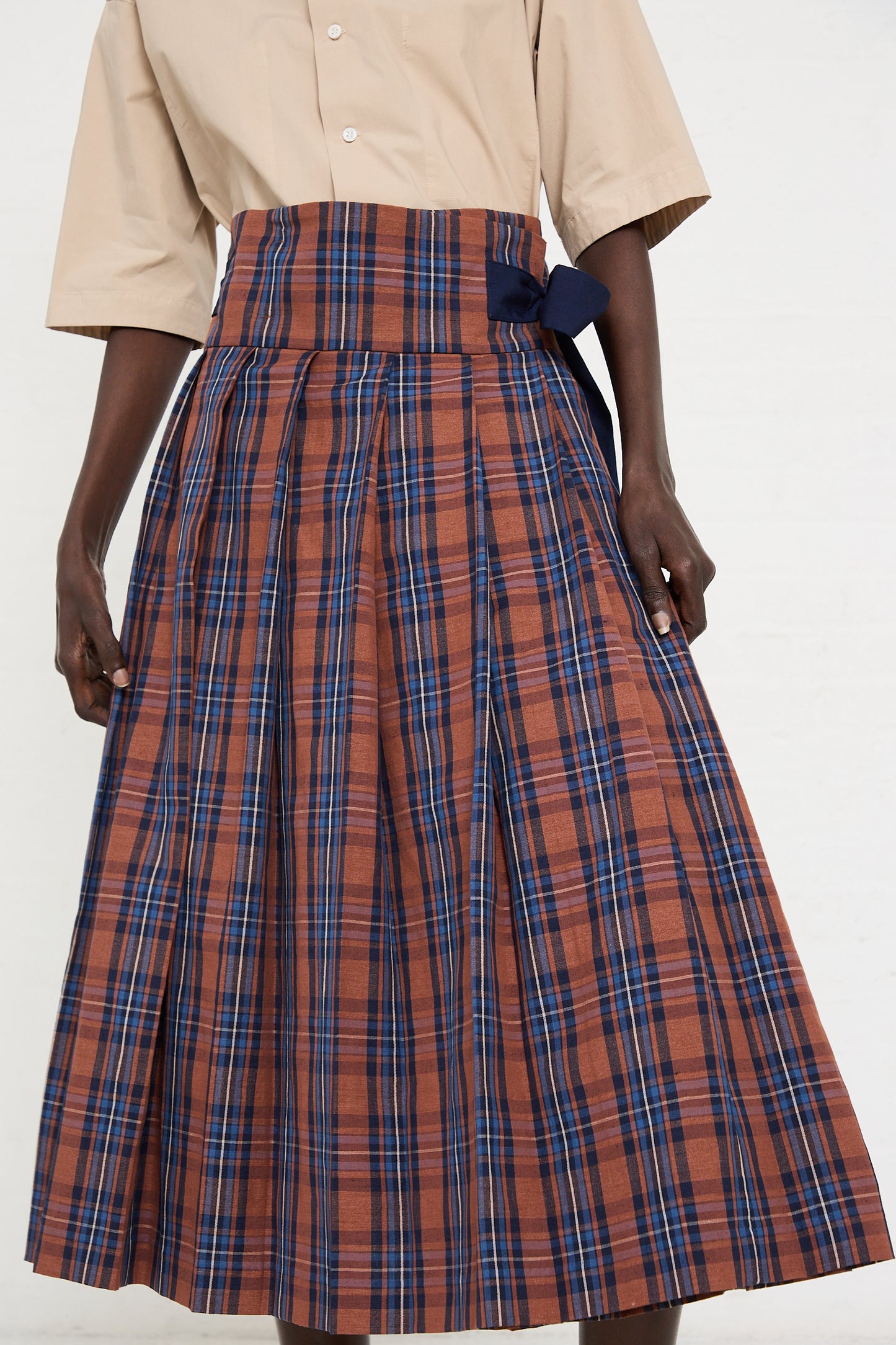 Person wearing a beige shirt and a high-waisted, pleated, ankle-length wrap skirt (Cotton Linen Madras Plaid Cloth Pleated Wrap Maxi Skirt in Brick) by Toujours with a brown, blue, and gray plaid cotton/linen blend pattern.