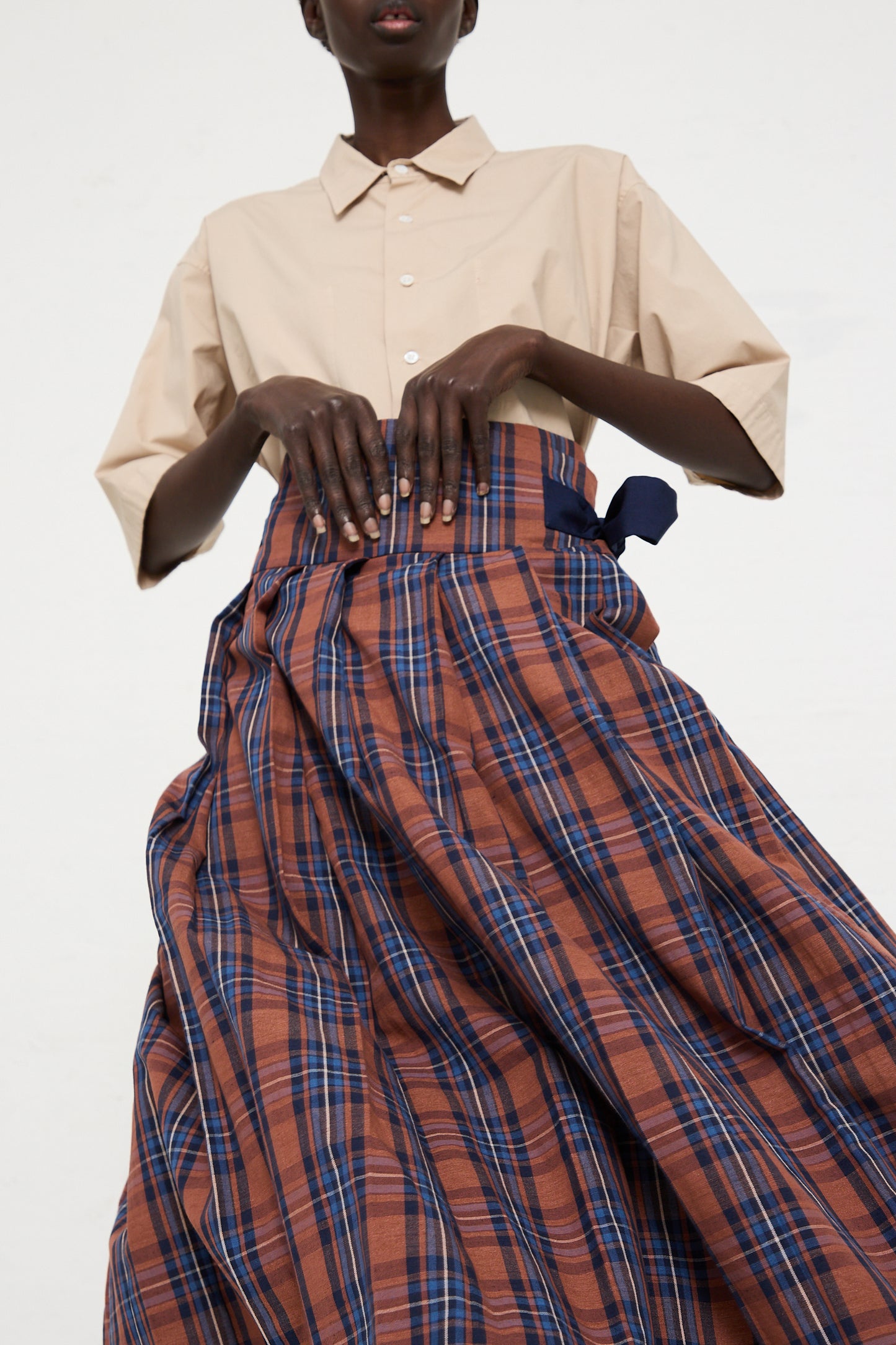 Person wearing a beige short-sleeve button-up shirt paired with the Toujours Cotton Linen Madras Plaid Cloth Pleated Wrap Maxi Skirt in Brick.