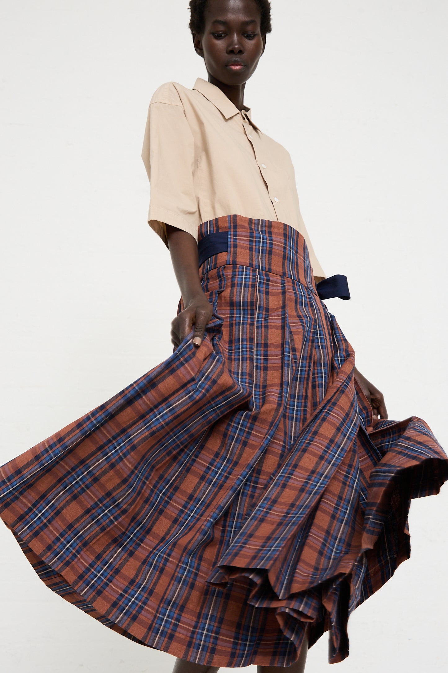 A person is wearing a beige short-sleeve shirt and a Cotton Linen Madras Plaid Cloth Pleated Wrap Maxi Skirt in Brick by Toujours, standing against a plain white background.