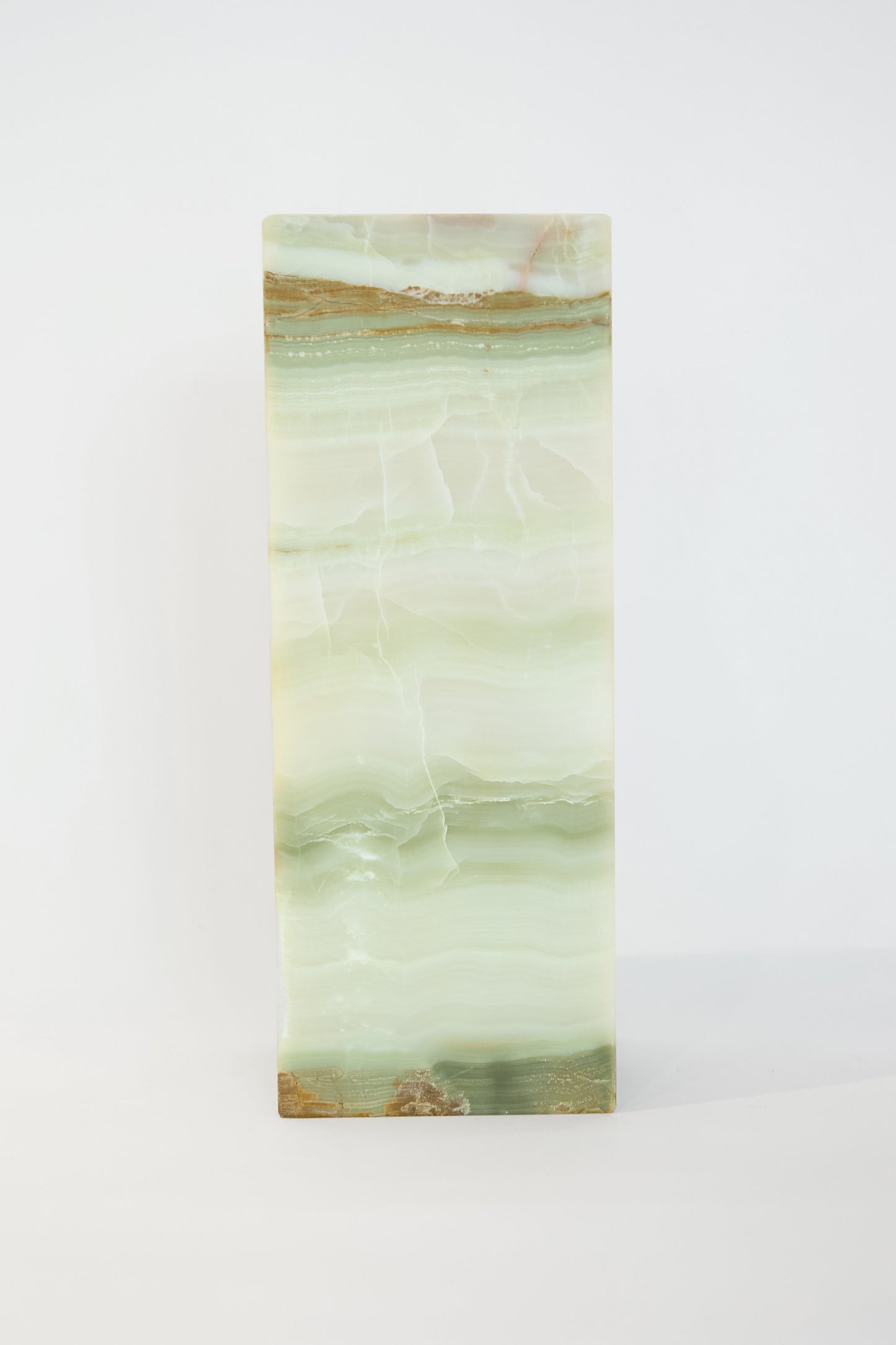 A Travel Find Green Onyx Lamp, featuring light green hues with subtle brown and white veins, stands vertically against a plain white background.