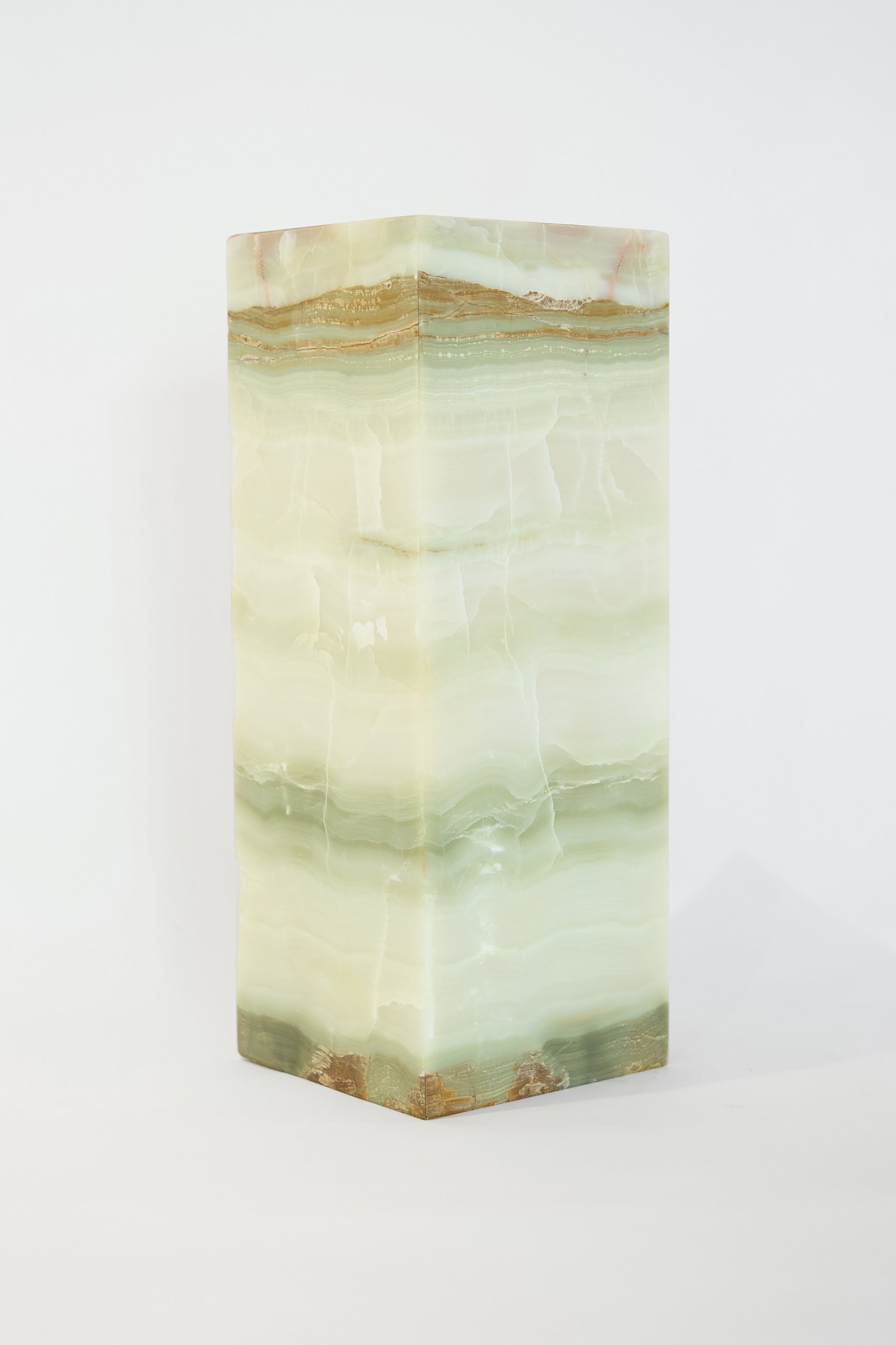 The Green Onyx Lamp by Travel Find is a tall, rectangular column crafted from green and white multi-layered Mexican banded onyx, showcasing a natural, swirled pattern.