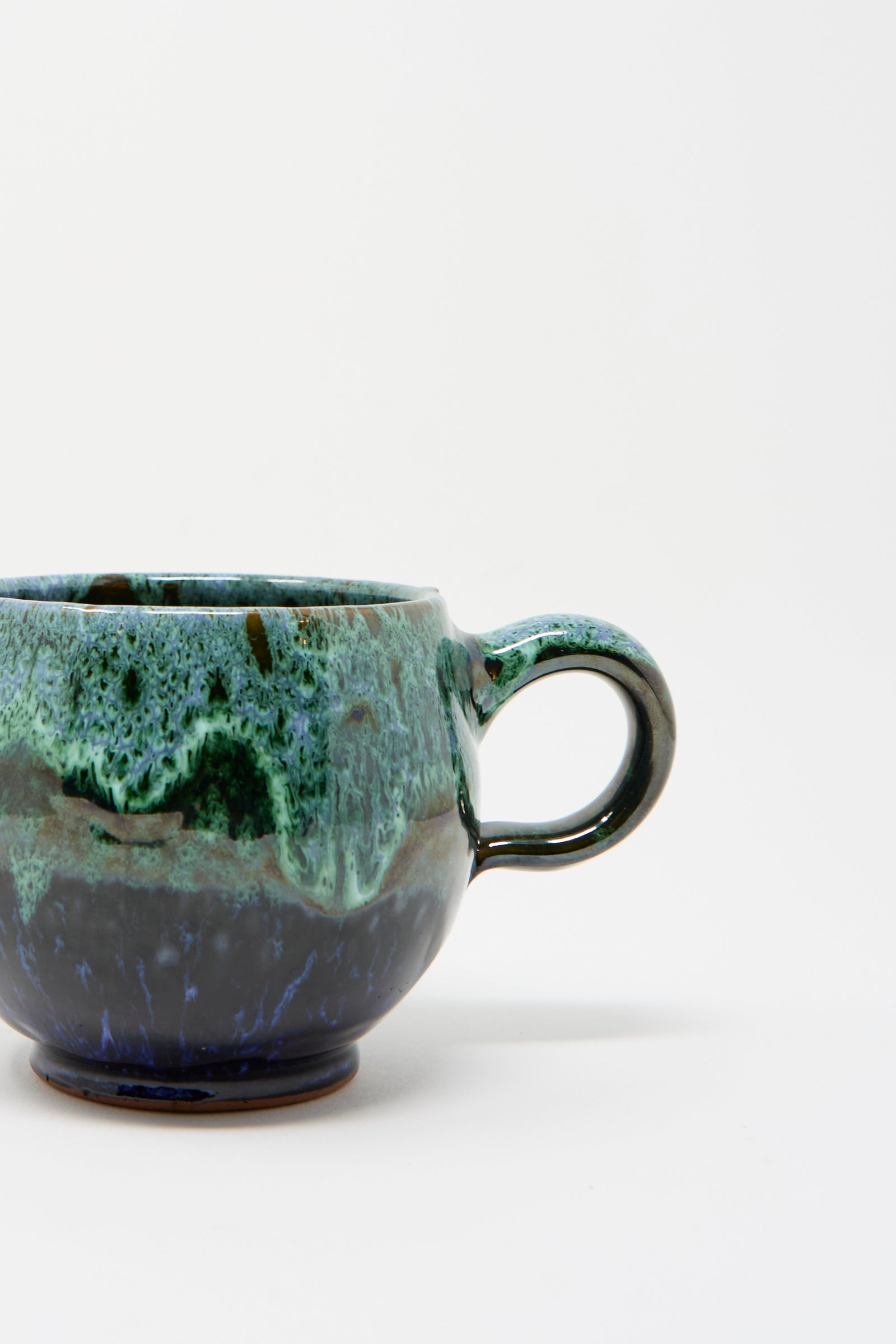 Showcased against a plain white background, the Handmade Mug in Green and Blue by Travel Find features glossy green and blue glaze.