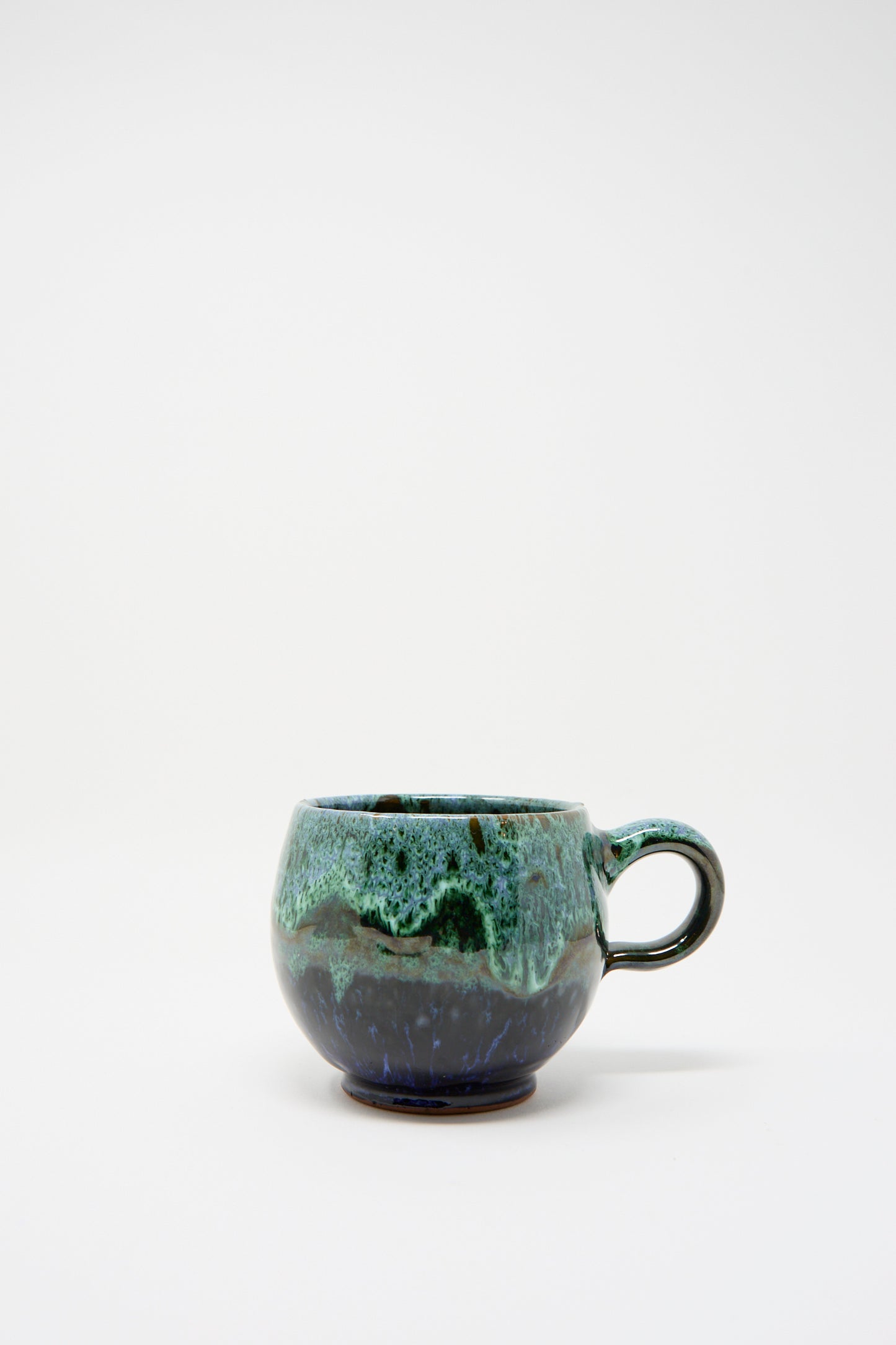 The Handmade Mug in Green and Blue by Travel Find showcases a round design with a single handle, featuring a green and blue glaze on a light background that evokes traditional Moroccan artistry.