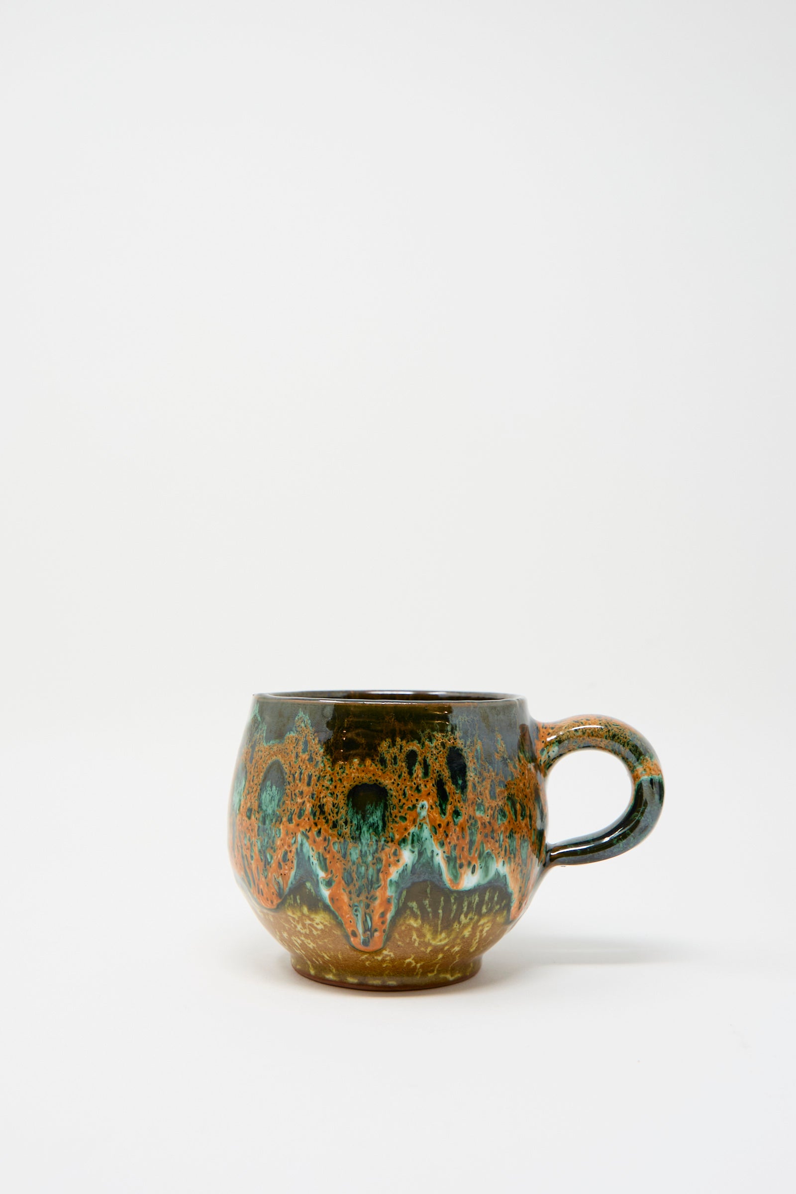 Discover the Handmade Mug in Green Orange Multi by Travel Find, showcasing an abstract, multicolored glaze inspired by traditional Moroccan artistry, on a plain white background.