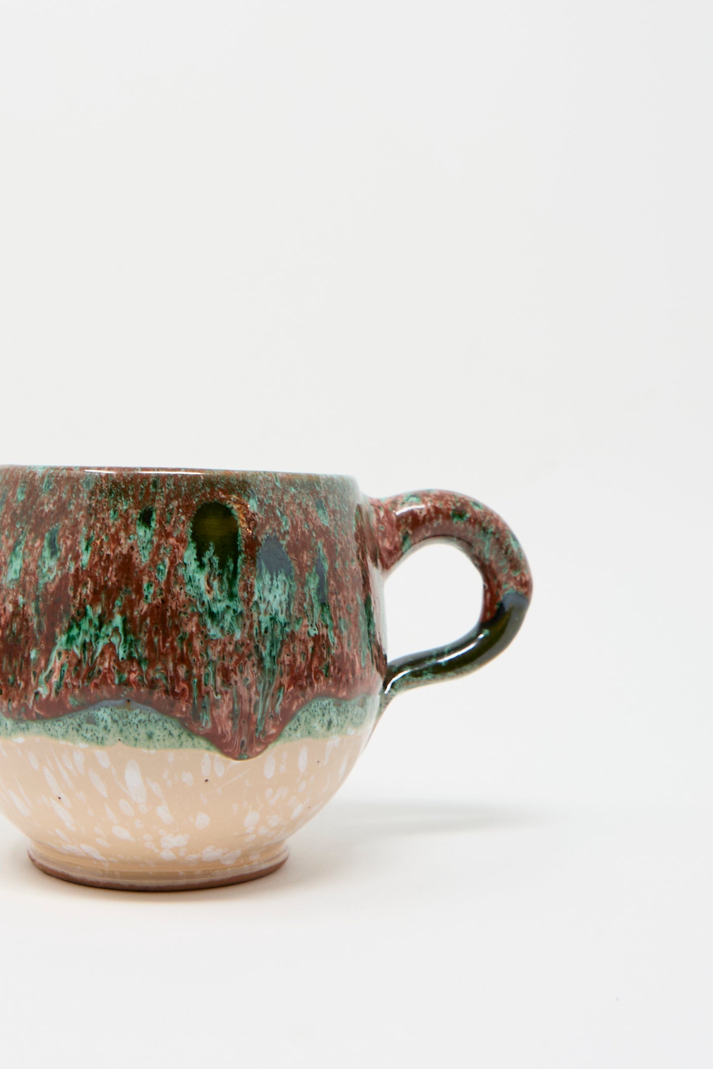 The "Handmade Mug in Red Multi" by Travel Find features a stunning multi-color glaze with textured green and red on the upper half and handle, complemented by a speckled beige bottom, standing out against a plain white background.