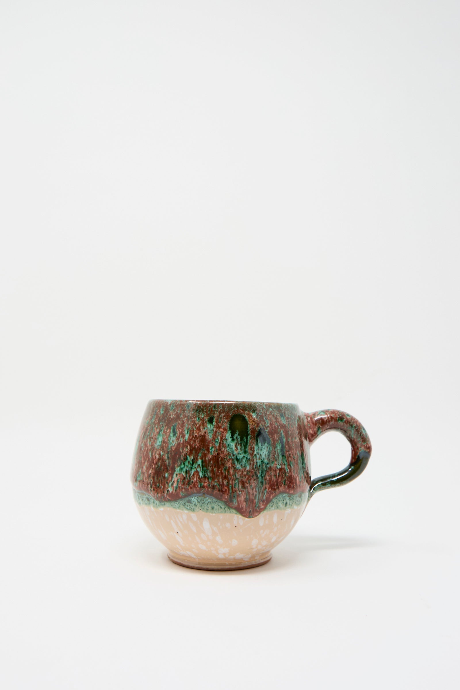 Handmade Mug in Red Multi by Travel Find, showcasing a textured multicolored glaze in earthy tones with a round base and curved handle, set against a white background.