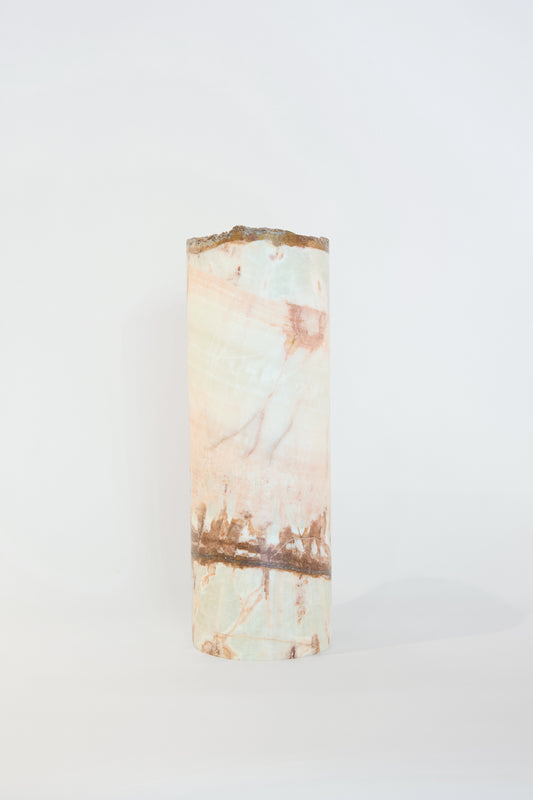 A cylindrical log of Travel Find's Pink Onyx Lamp, showcasing its pale green and pink hues, displayed against a plain white background.