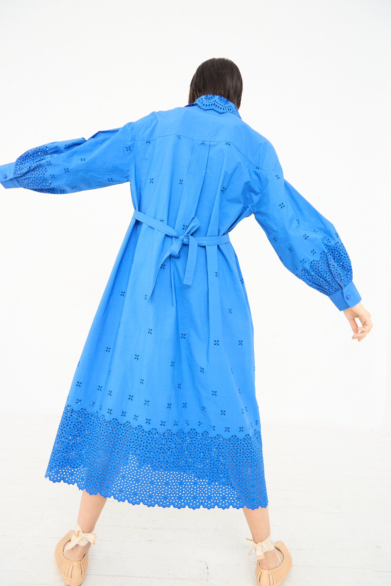 Woman in a Ulla Johnson Adette Dress in Cobalt with eyelet design cut-out patterns, seen from the back, twirling.