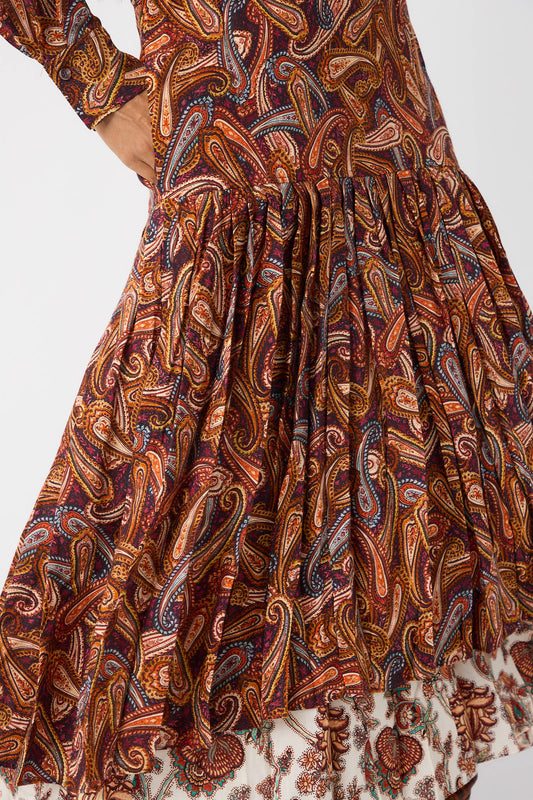 Close-up of a person wearing the Adira Dress in Bergamot by Ulla Johnson. This wool twill turtleneck dress features a colorful paisley pattern, a gathered skirt with intricate details, and a blend of warm and cool tones.