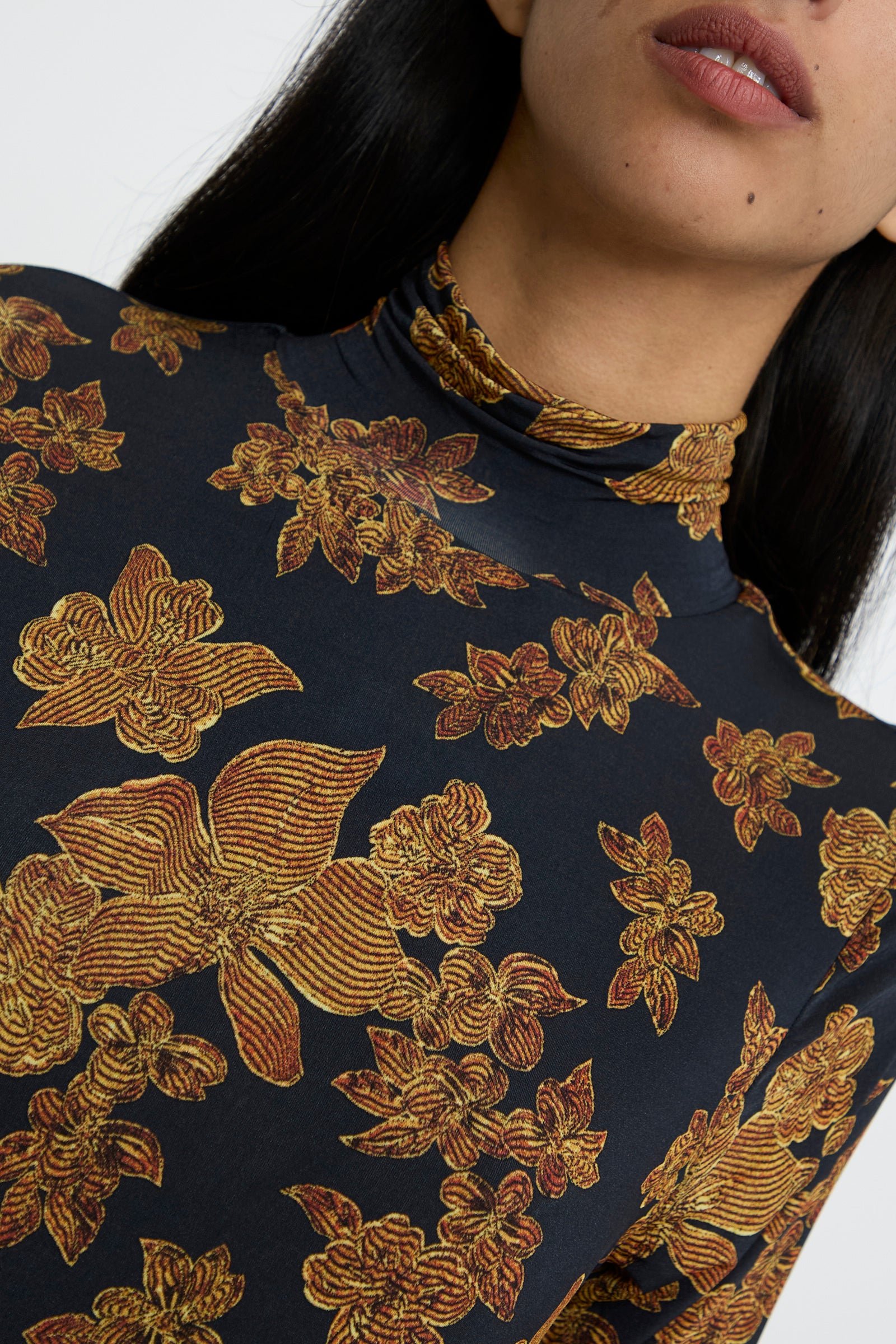 Close-up of a person wearing the Amaya Dress in Onyx by Ulla Johnson, featuring an intricate orange floral pattern. The image focuses on the upper torso and partial view of the face. 