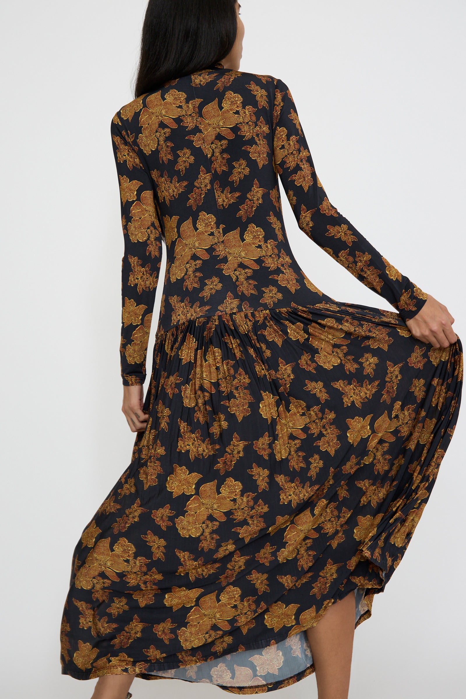 A person wearing the Amaya Dress in Onyx by Ulla Johnson poses with their back to the camera, holding the sides of the long-sleeve, floral pattern maxi dress.