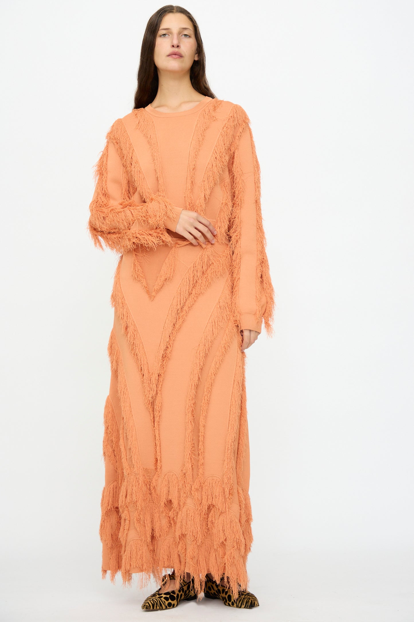A woman stands against a white background wearing the Ulla Johnson Astrid Maxi Skirt in Tulip, featuring textured fringe and patterned jacquard accents, paired with animal print shoes.