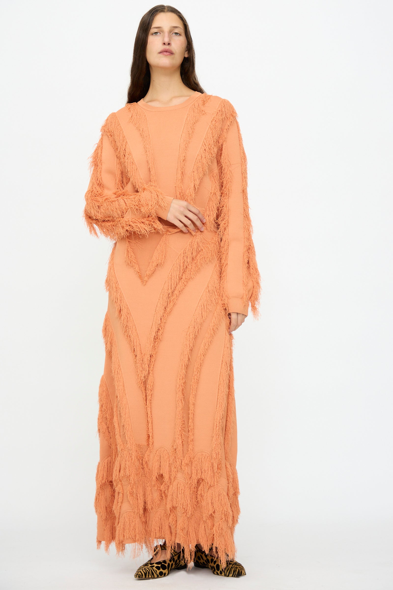 A woman stands against a white background wearing the Ulla Johnson Astrid Maxi Skirt in Tulip, featuring textured fringe and patterned jacquard accents, paired with animal print shoes.