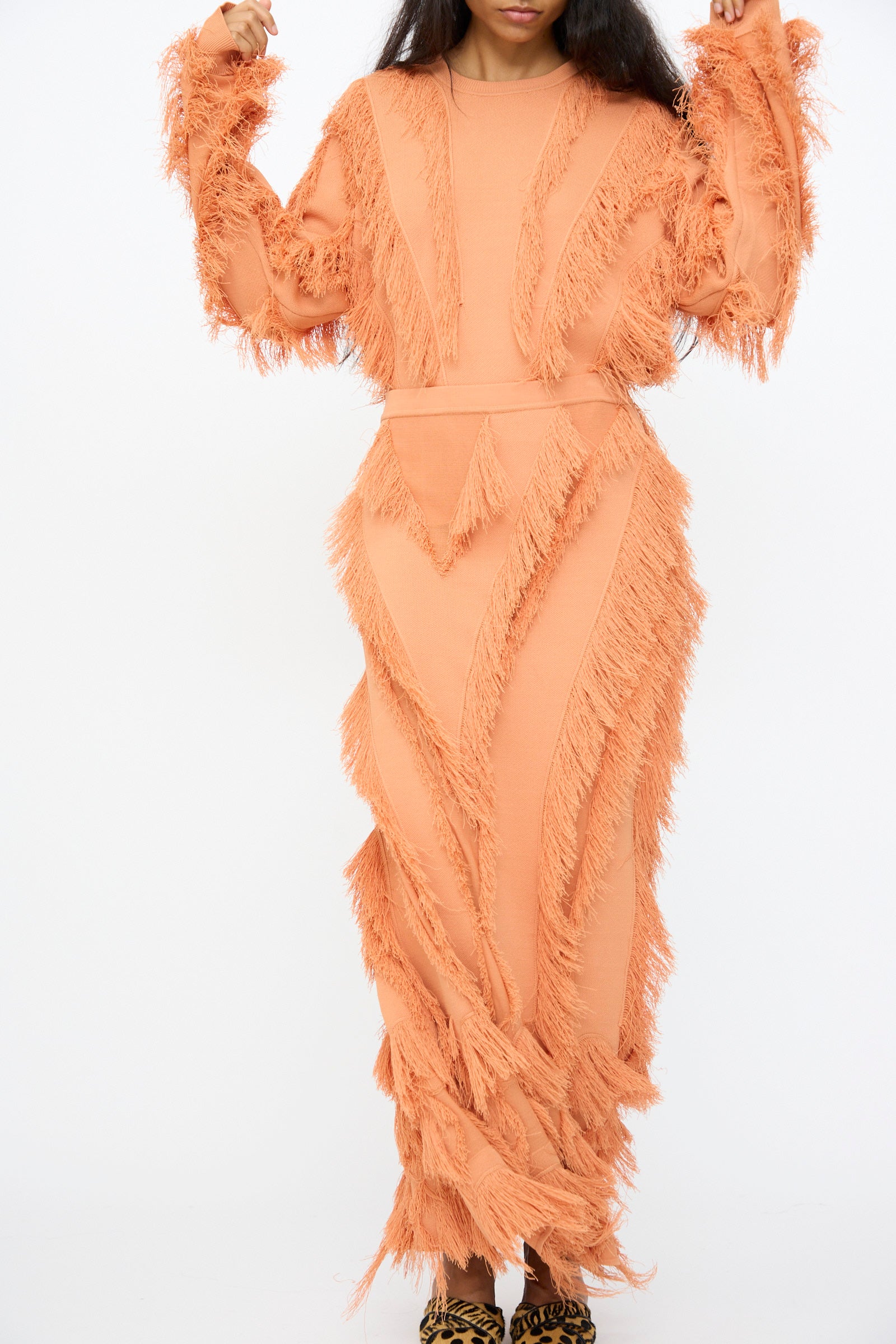 A person, with only their lower face visible, stands against a white background wearing the Ulla Johnson Astrid Maxi Skirt in Tulip, a long jacquard design featuring fringe details.