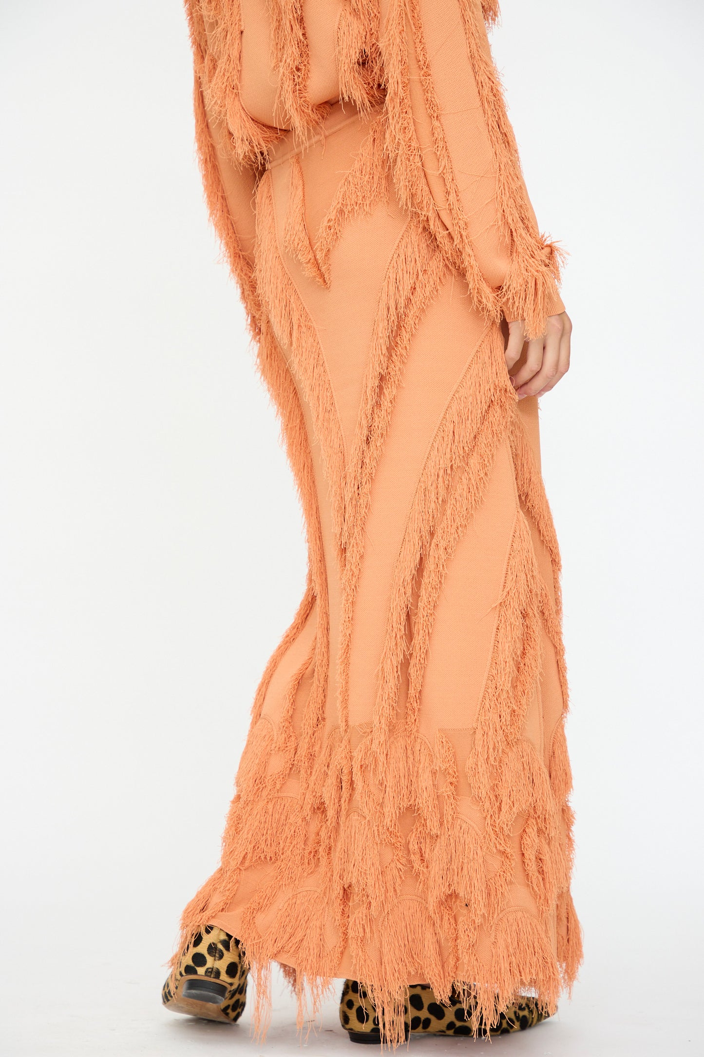 Wearing the Astrid Maxi Skirt in Tulip by Ulla Johnson, this look pairs a fringe-patterned peach skirt with an elastic waist and matching top; leopard print shoes peek out from beneath the flowing maxi.