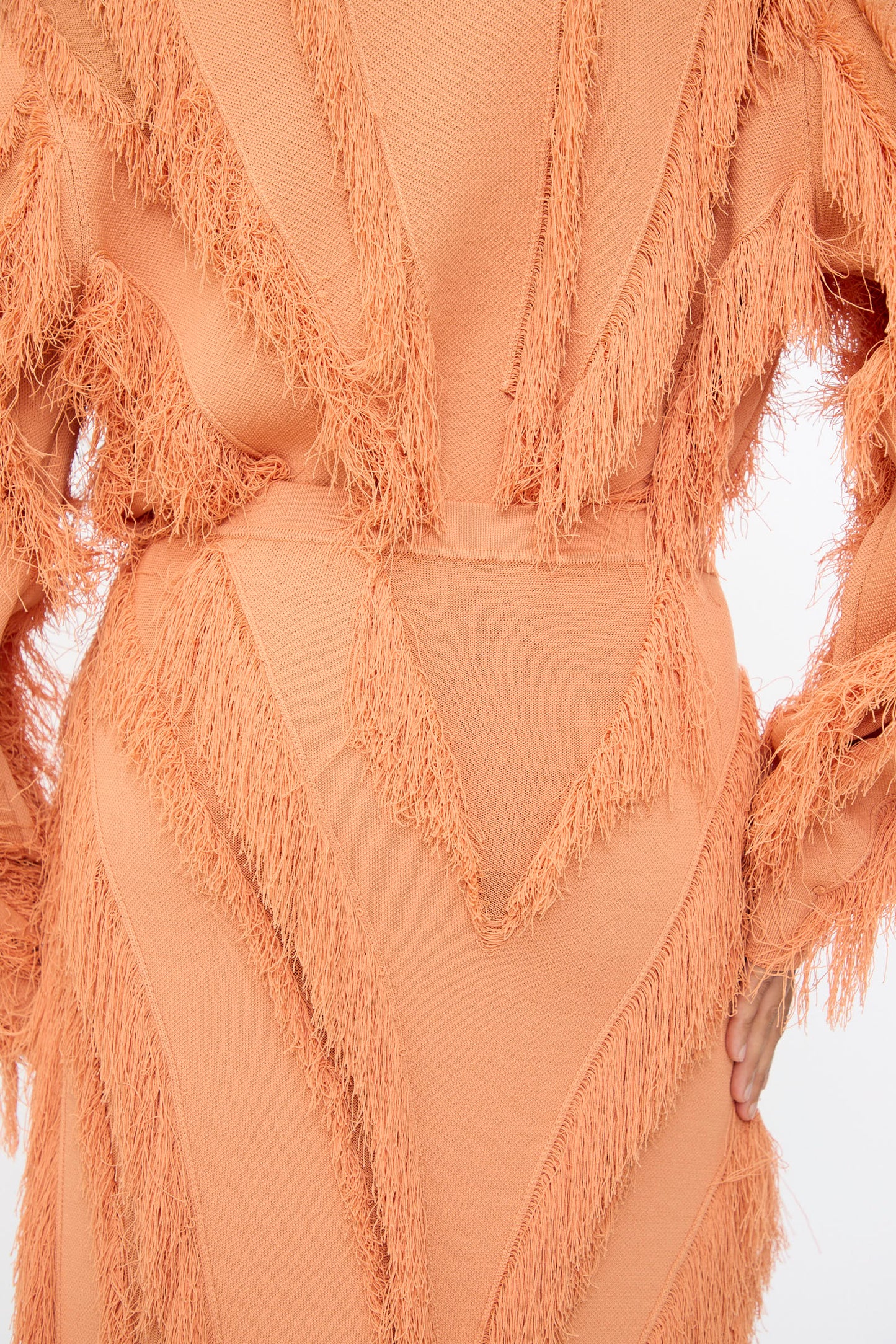 A person models the Ulla Johnson Astrid Maxi Skirt in Tulip, a textured peach jacquard skirt with fringed zigzag patterns, shown from the back with one hand on their hip.