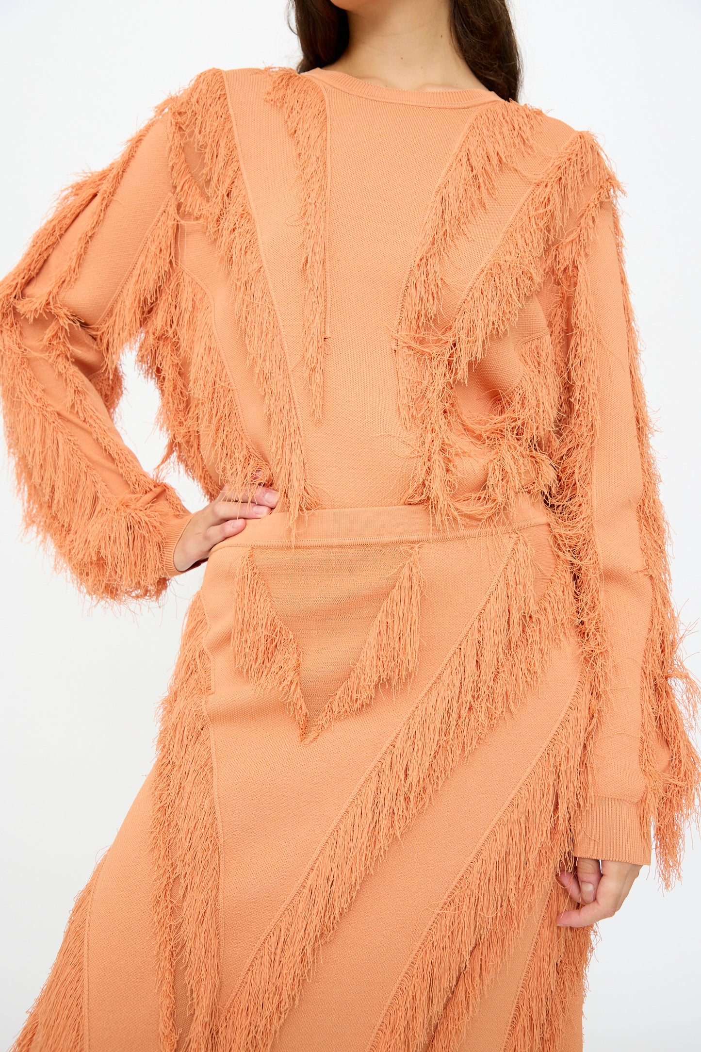 A woman poses with one hand on her hip, wearing the Ulla Johnson Astrid Maxi Skirt in Tulip, featuring textured fringe details and an elasticated waist.
