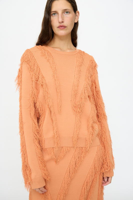 A woman models the Ulla Johnson Aubree Knit Pullover in Tulip—a peach-hued sweater with a textured fringe pattern—standing against a plain white background.