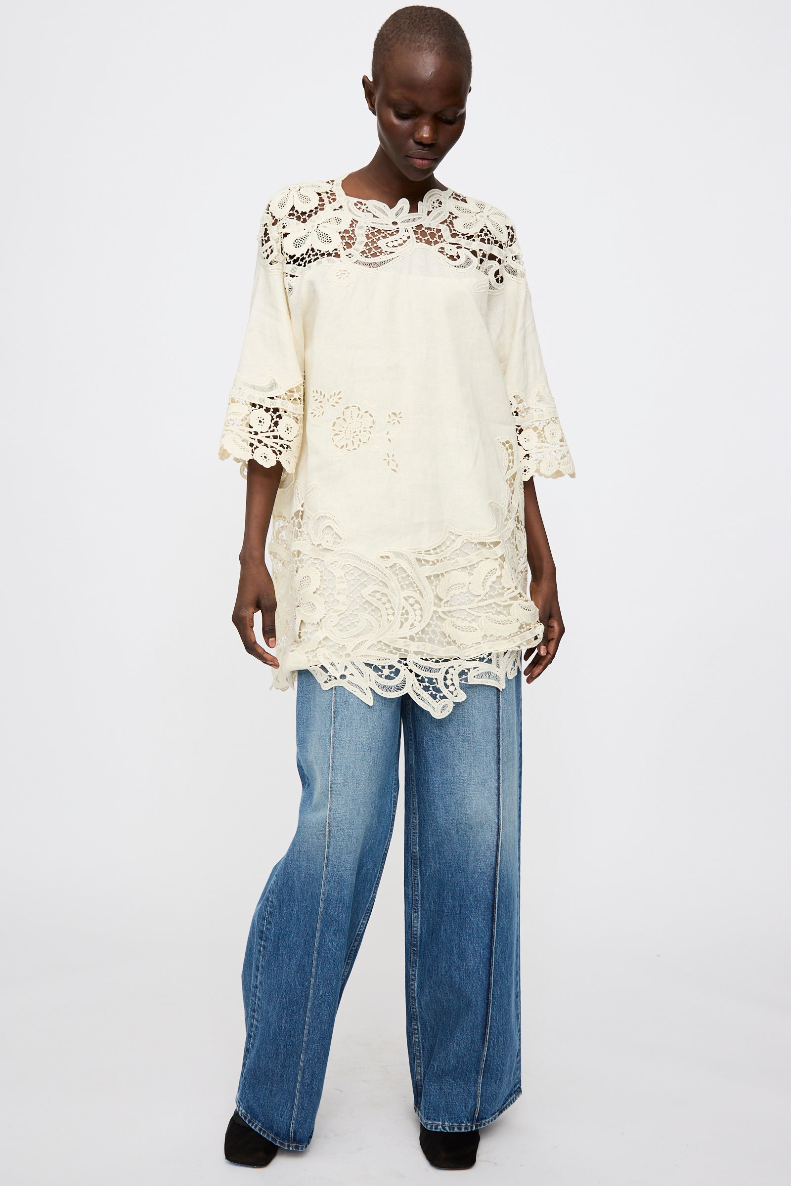 A person wears the Ulla Johnson Botanical Linen Lace Brinna Top in Pristine with wide-leg blue jeans, posed against a plain white background.