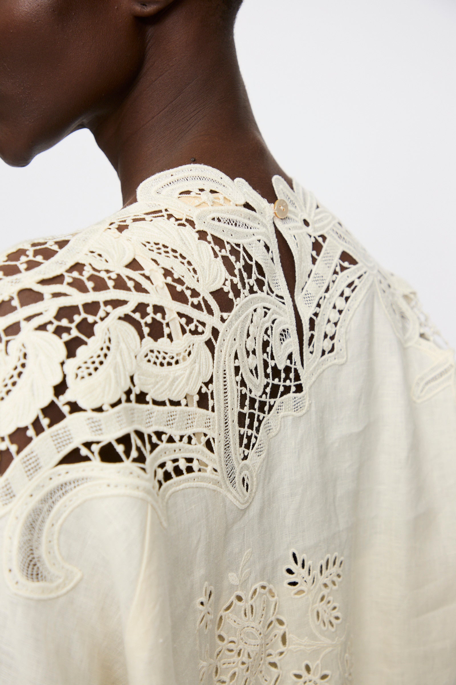 Close-up of the Ulla Johnson Botanical Linen Lace Brinna Top in Pristine, showing detailed floral lace and embroidery on cream linen, worn by a short-haired model against a plain background.