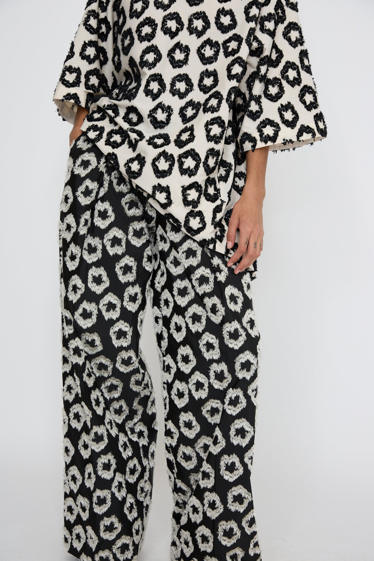 A person is wearing the Cai Pant in Eclipse from Ulla Johnson, featuring a black and white floral pattern, crafted from an Italian cotton/linen blend, set against a plain background.