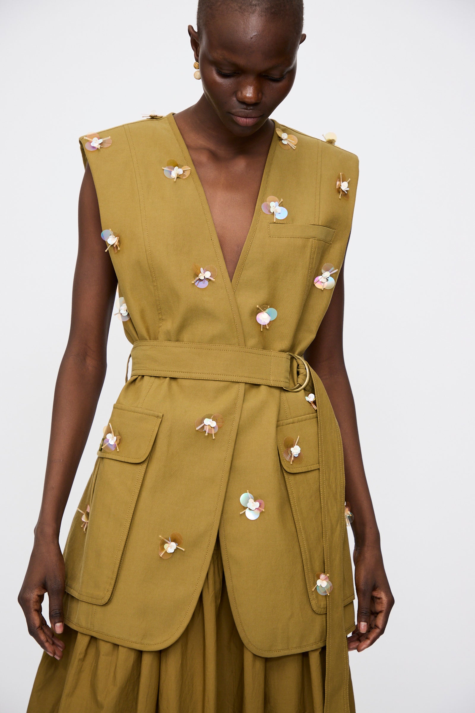 A person wears the Ulla Johnson Embroidered Cotton Twyla Vest in Lichen, featuring paillette florals and large front pockets, paired with a matching skirt.