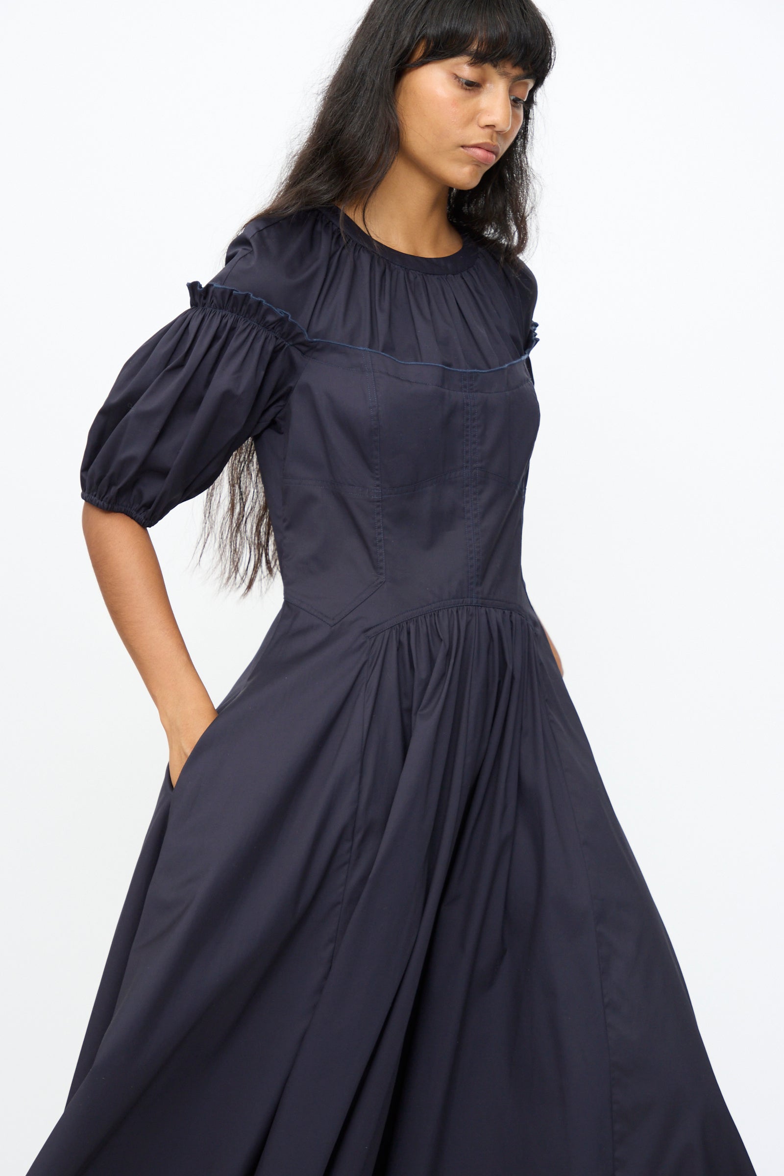 A woman wears the Ulla Johnson Estelle Dress in Midnight—an ankle-length, puff-sleeve organic cotton dress with a gathered waist and yoke detail—while standing against a plain white background.