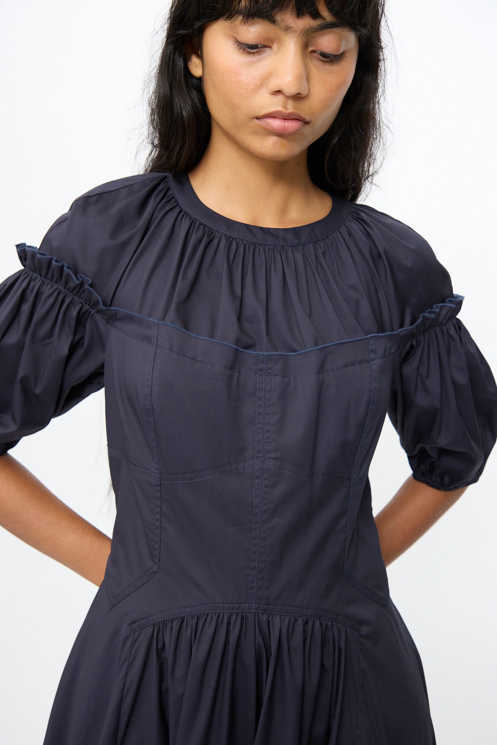 A woman wears the Ulla Johnson Estelle Dress in Midnight, featuring puff sleeves, gathered details, and a subtle corset silhouette, standing against a plain white background.