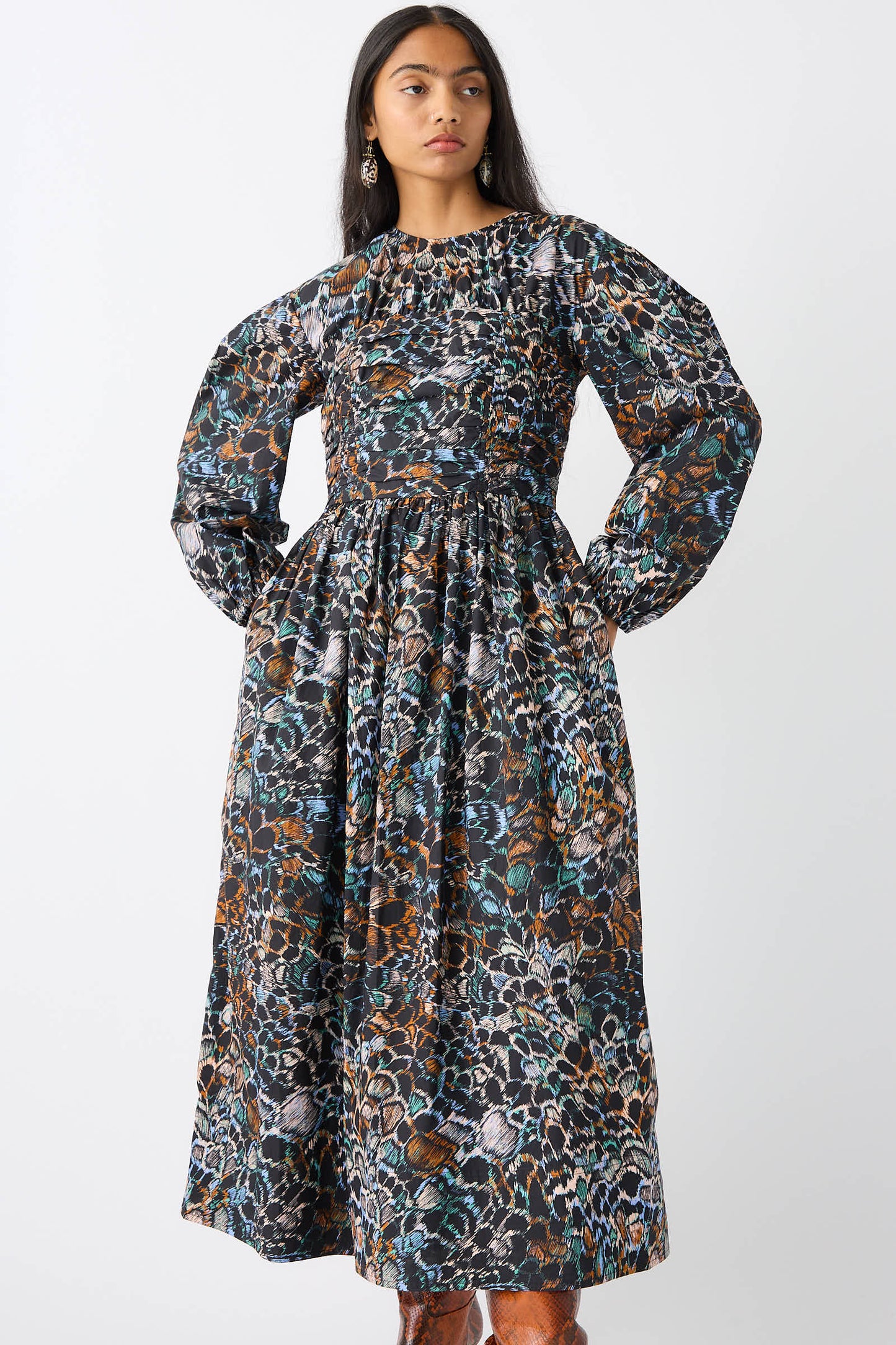 A woman wearing the Ulla Johnson Estyne Dress in Starling, a long-sleeved, ankle-length garment made from cotton poplin with an abstract, multi-colored pattern, stands against a plain white background.