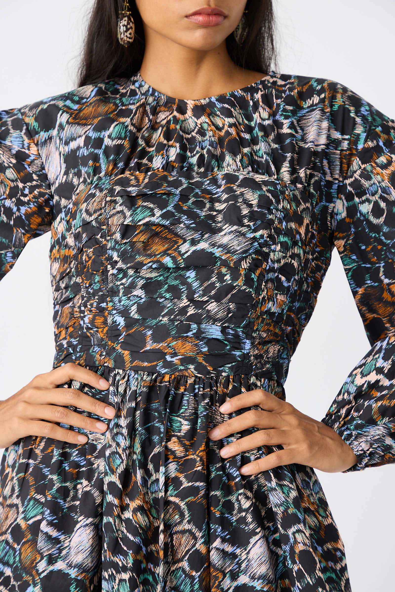 A person in the Ulla Johnson Estyne Dress in Starling, featuring a graphic multicolored feather print and long sleeves, standing with hands on hips.