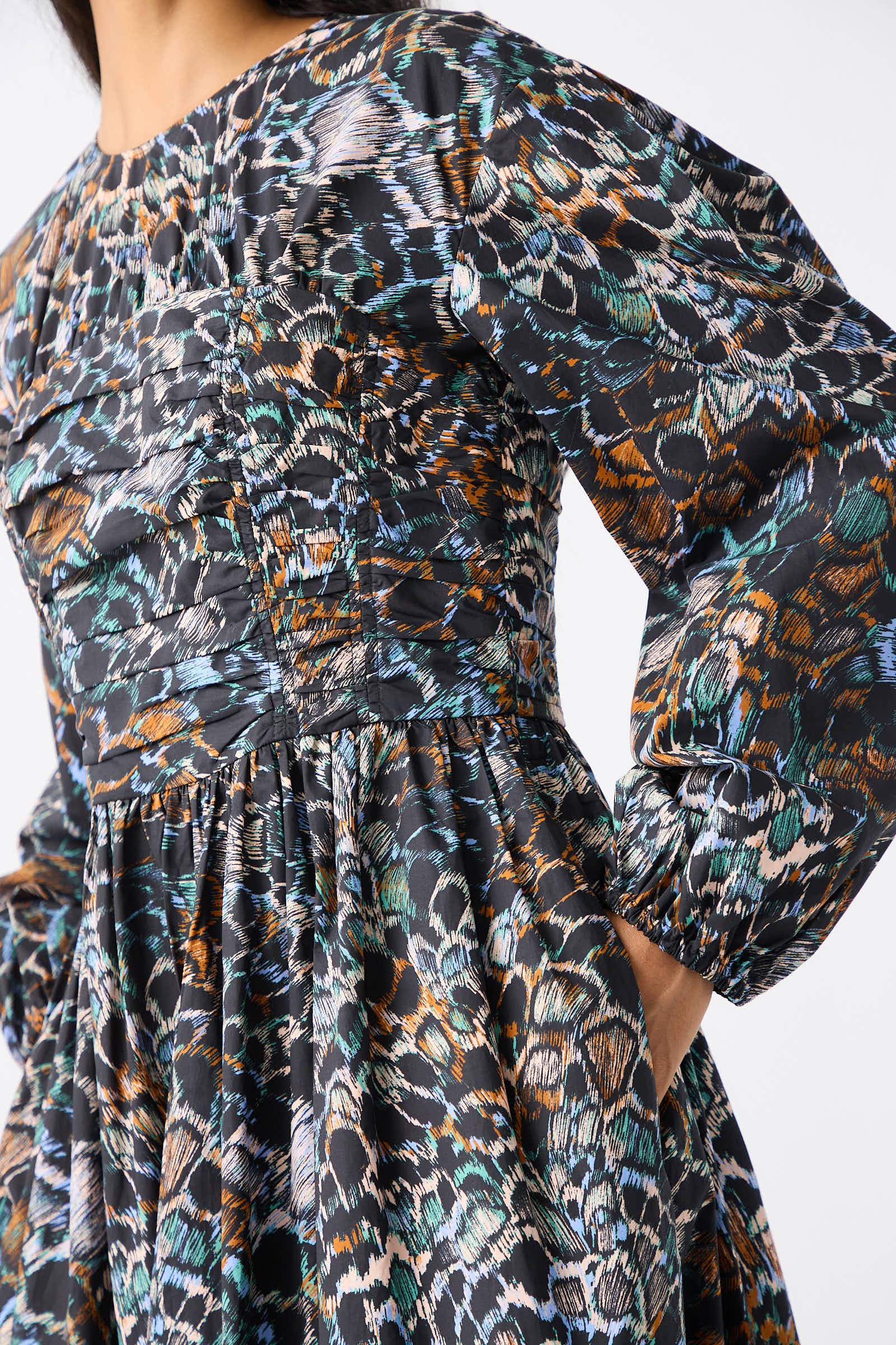 Close-up of a person wearing the Estyne Dress in Starling by Ulla Johnson. This long-sleeved cotton poplin dress features a graphic multicolored feather print pattern, gathered fabric details at the torso, and a flowing skirt.