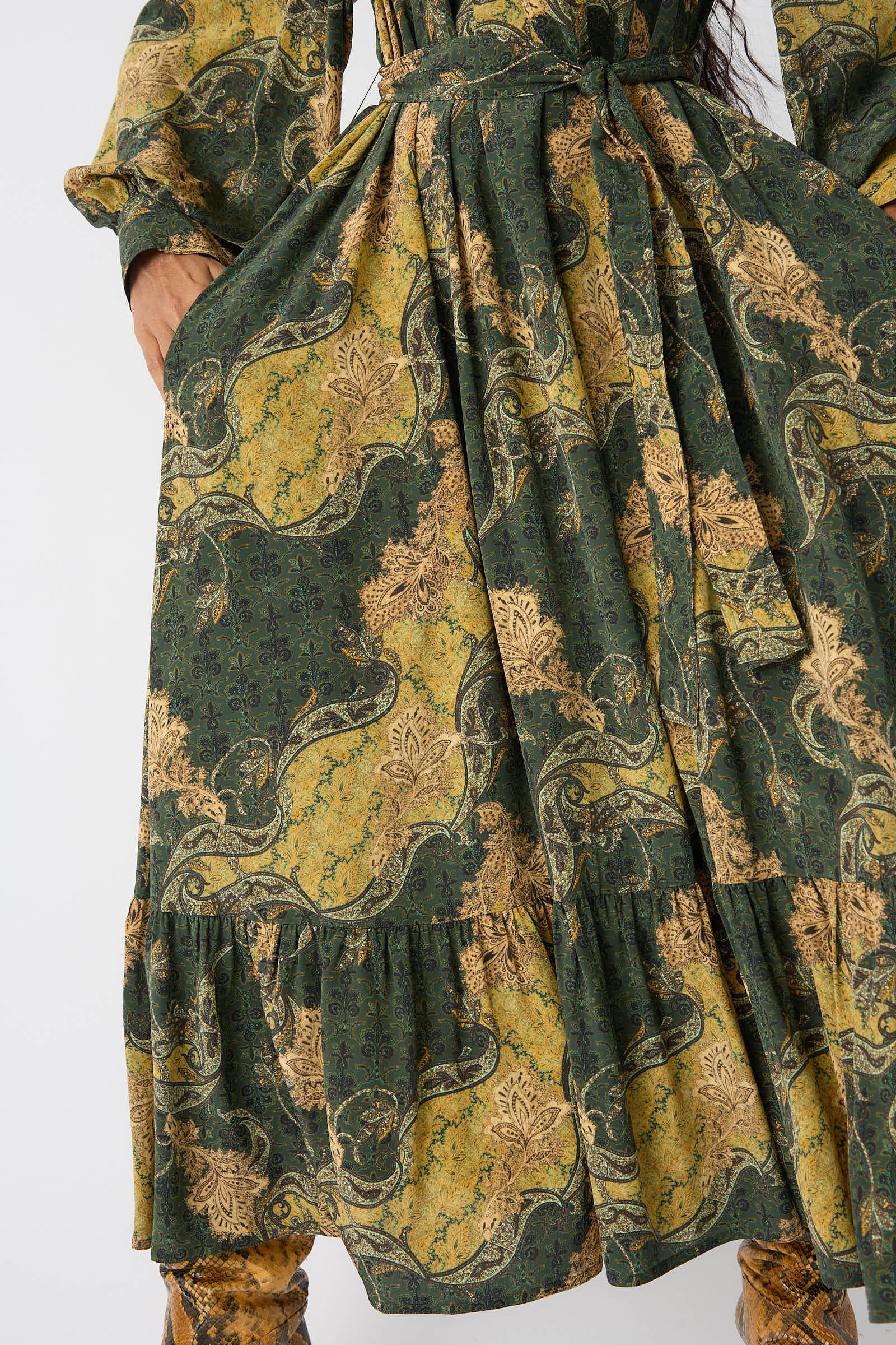 Close-up of a person wearing the Ulla Johnson Fianna Dress in Alpine, featuring a green and yellow floral paisley print, holding the sides of the skirt.