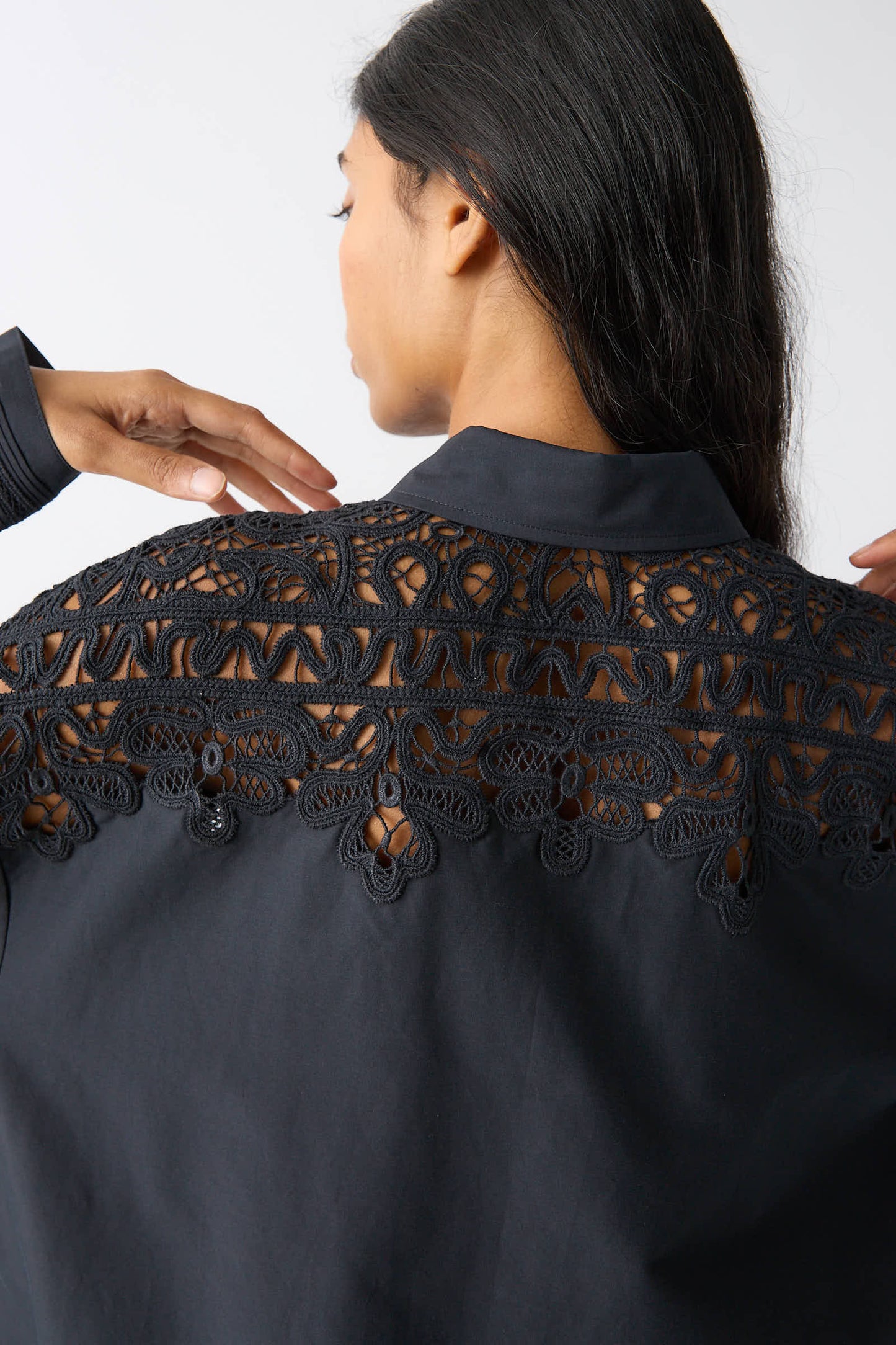 Back view of a person with long dark hair wearing the Ulla Johnson Harden Tunic in Noir, which features intricate Battenberg lace detailing on the upper back.