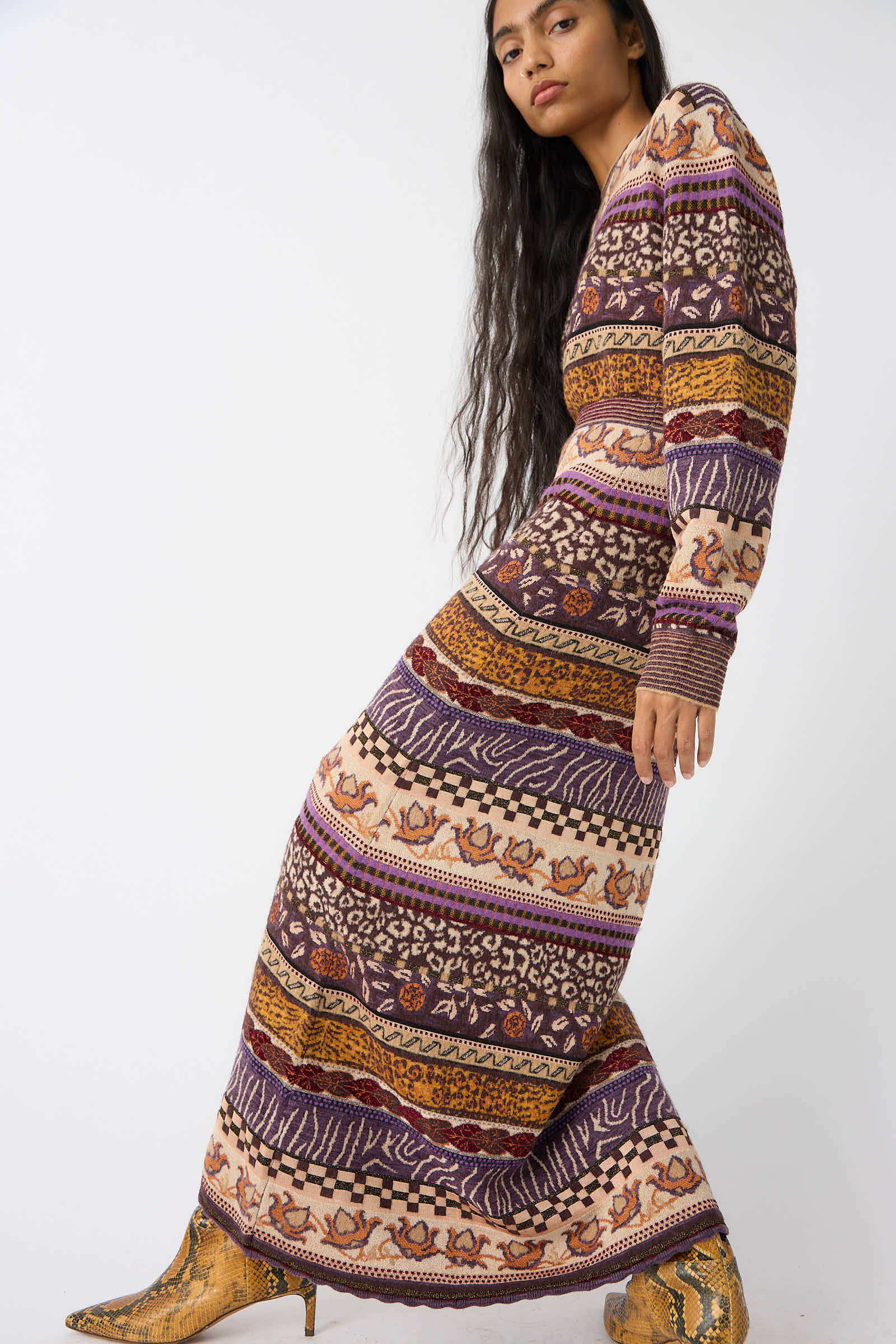 An individual in a long-sleeved, multicolored striped Helene Skirt in Woodland by Ulla Johnson with Fair Isle motifs and assorted patterns poses with one leg slightly forward, wearing high-heeled boots.