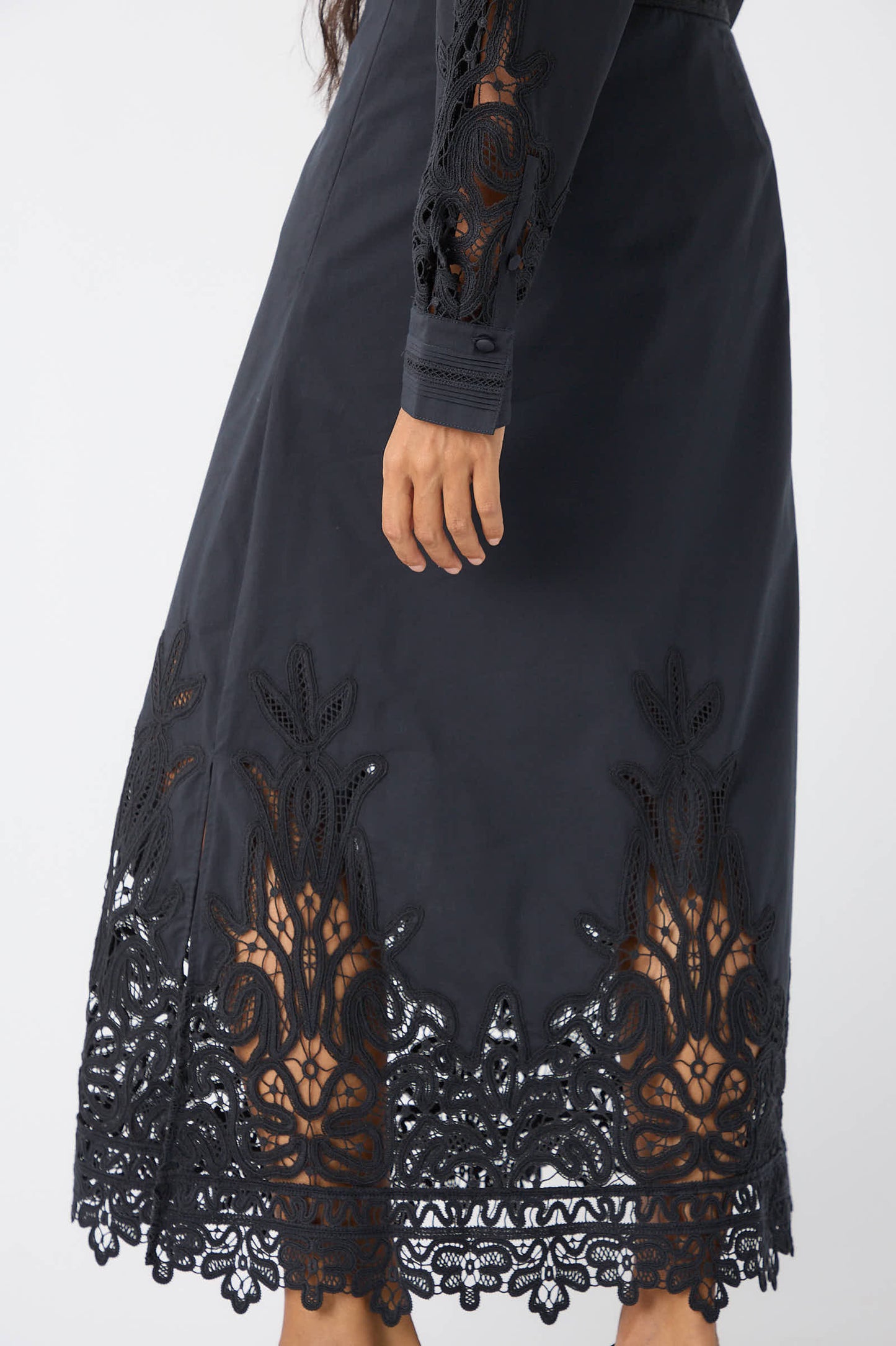 A person wearing the Ulla Johnson Karlyn Skirt in Noir, made from a luxurious cotton/silk blend with intricate Battenberg lace details on the sleeves and hem, standing against a plain background.