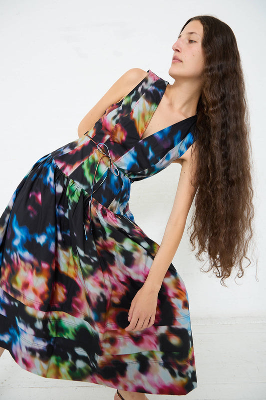 Person with long wavy hair wearing a sleeveless, colorful tie-dye cotton Ulla Johnson Kiran Dress in Aura, posing with a leaning posture against a plain white background.